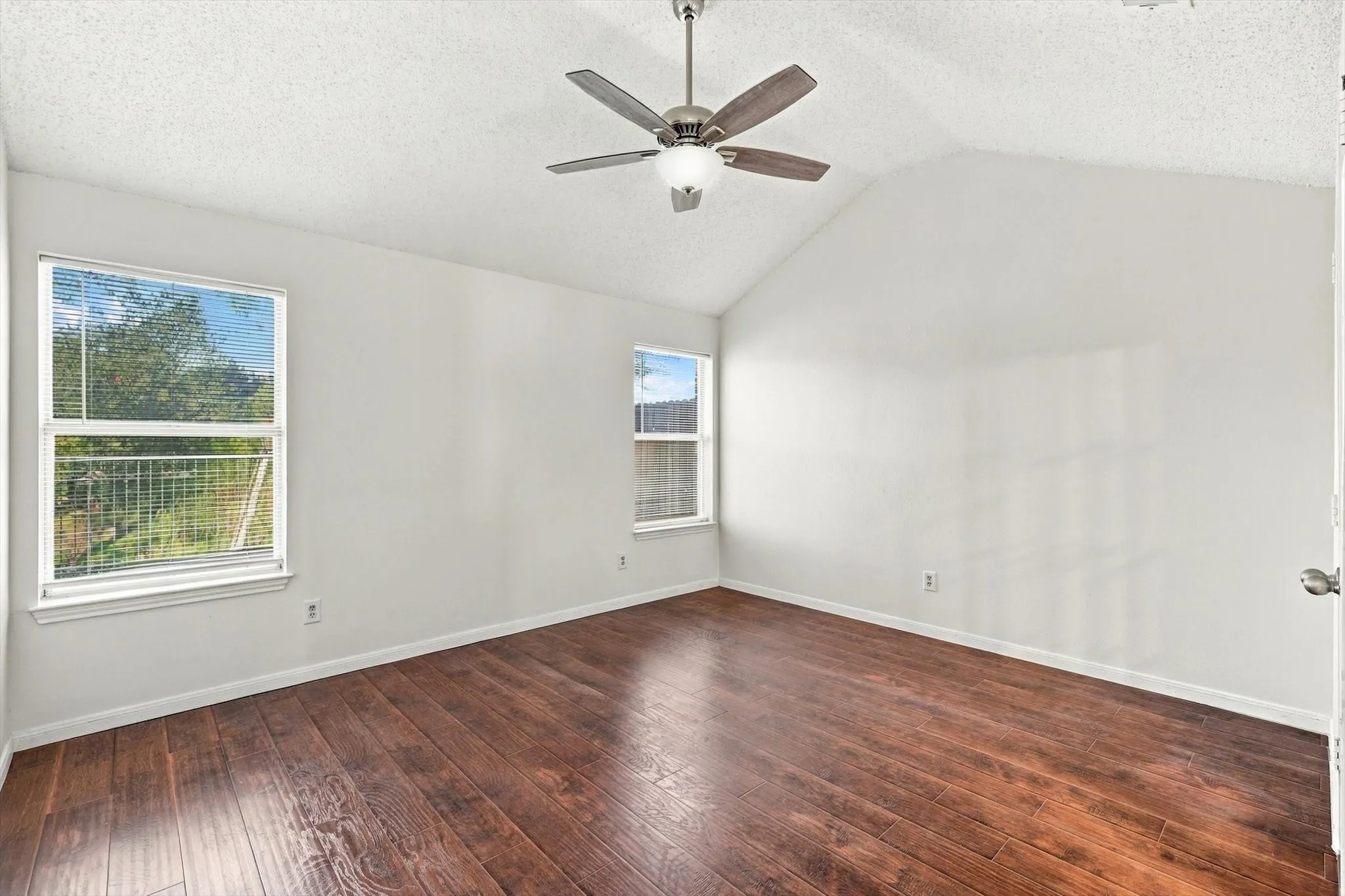 Vaulted ceilings, wood-finish flooring, two dual-pane windows, and a ceiling fan with integrated lighting