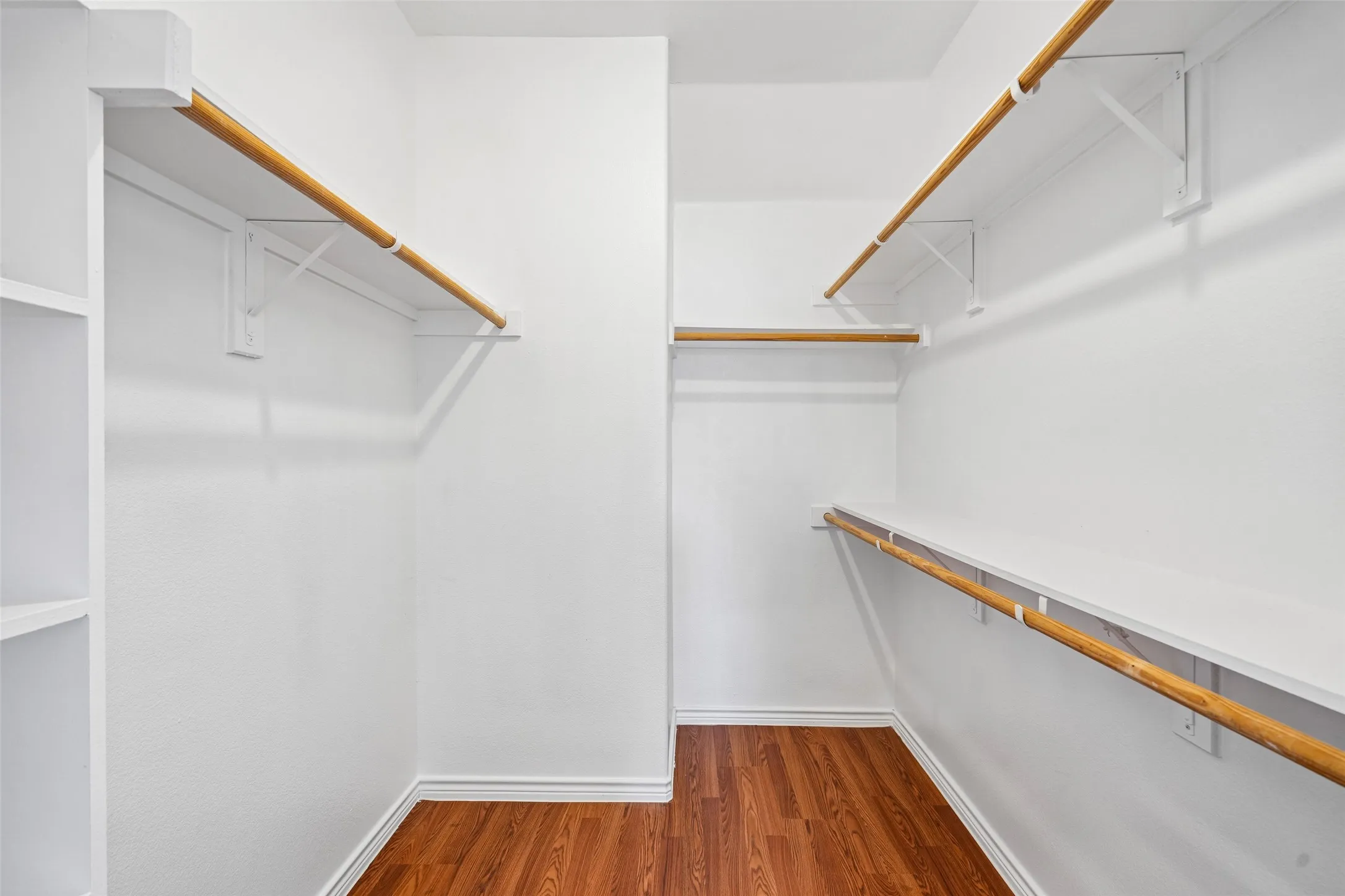 Walk-in closet featuring wood-finish flooring, built-in shelving, and tiered wooden hanging rods