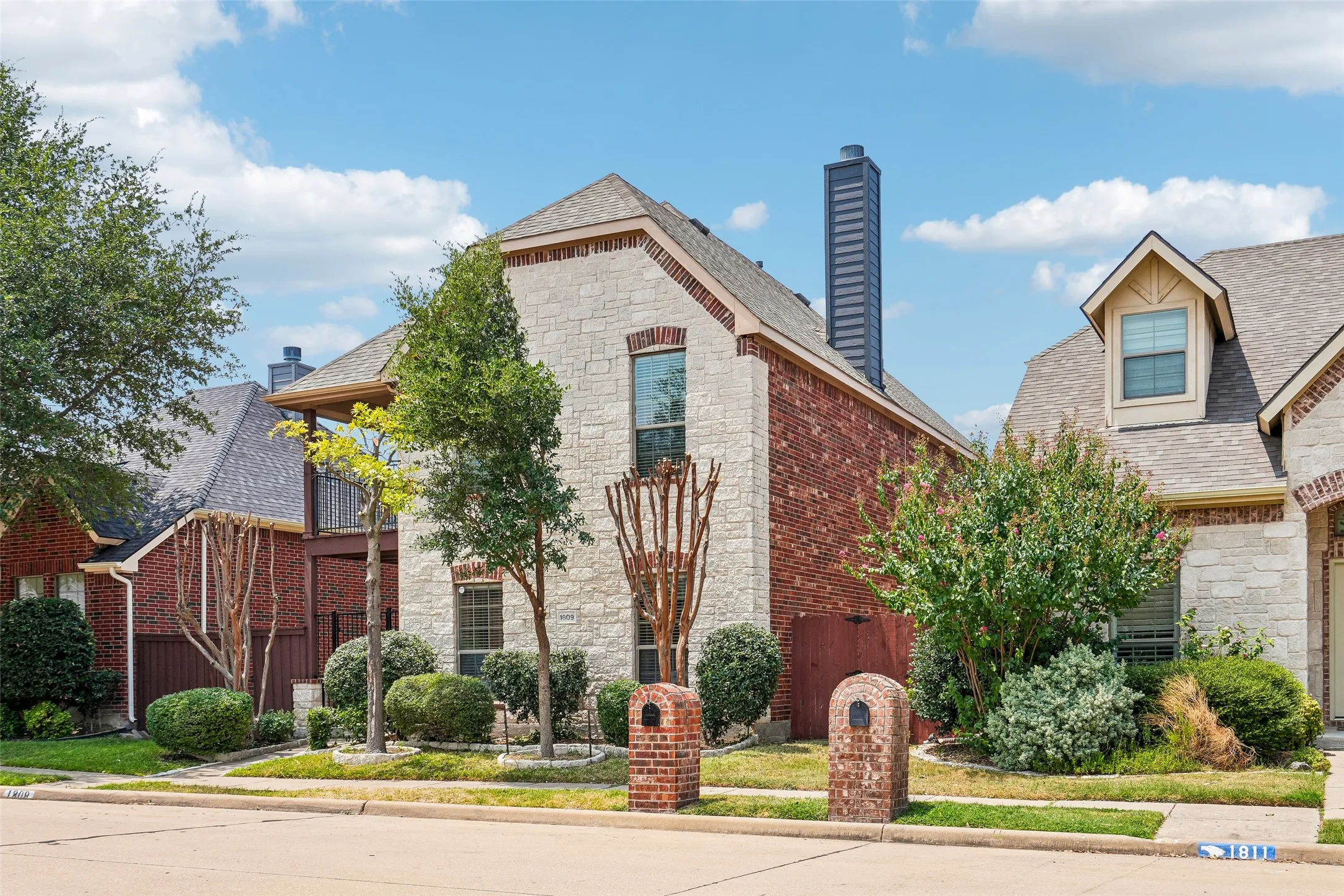 Two-story exterior featuring a brick and stone facade, a multi-gabled roofline, a tall metal chimney stack, and an elevated wooden balcony