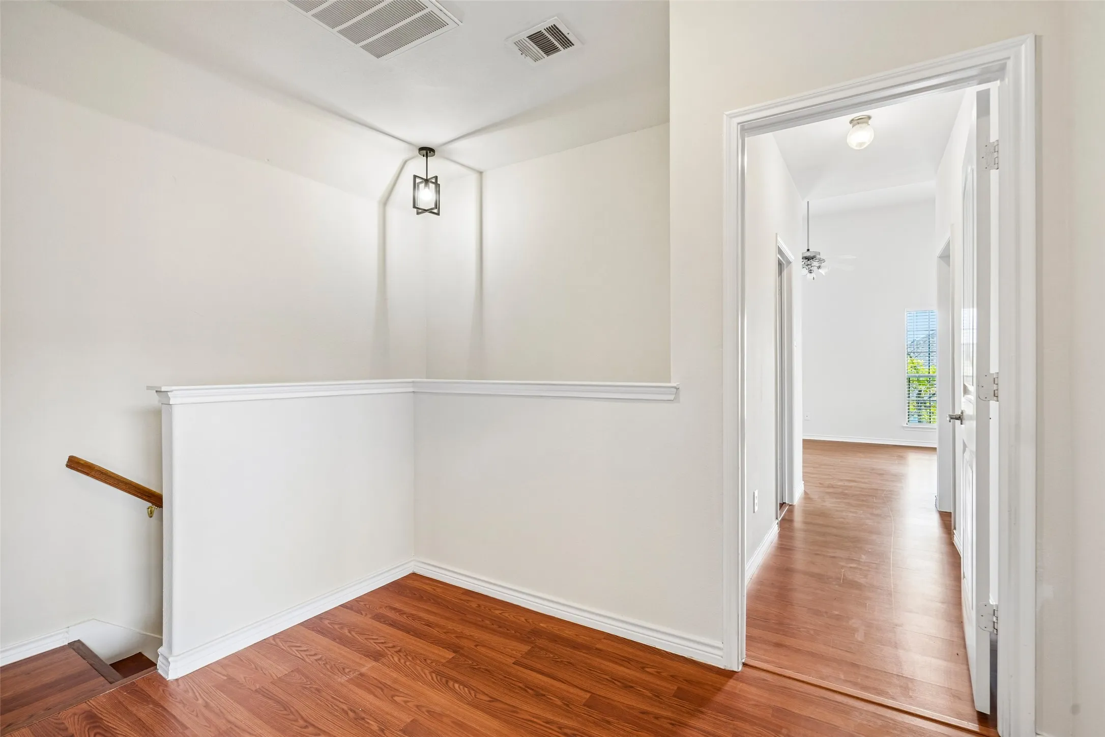 Landing area featuring wood-finish flooring, a wall-mounted cage-style light fixture, and a white half-wall with a wooden handrail