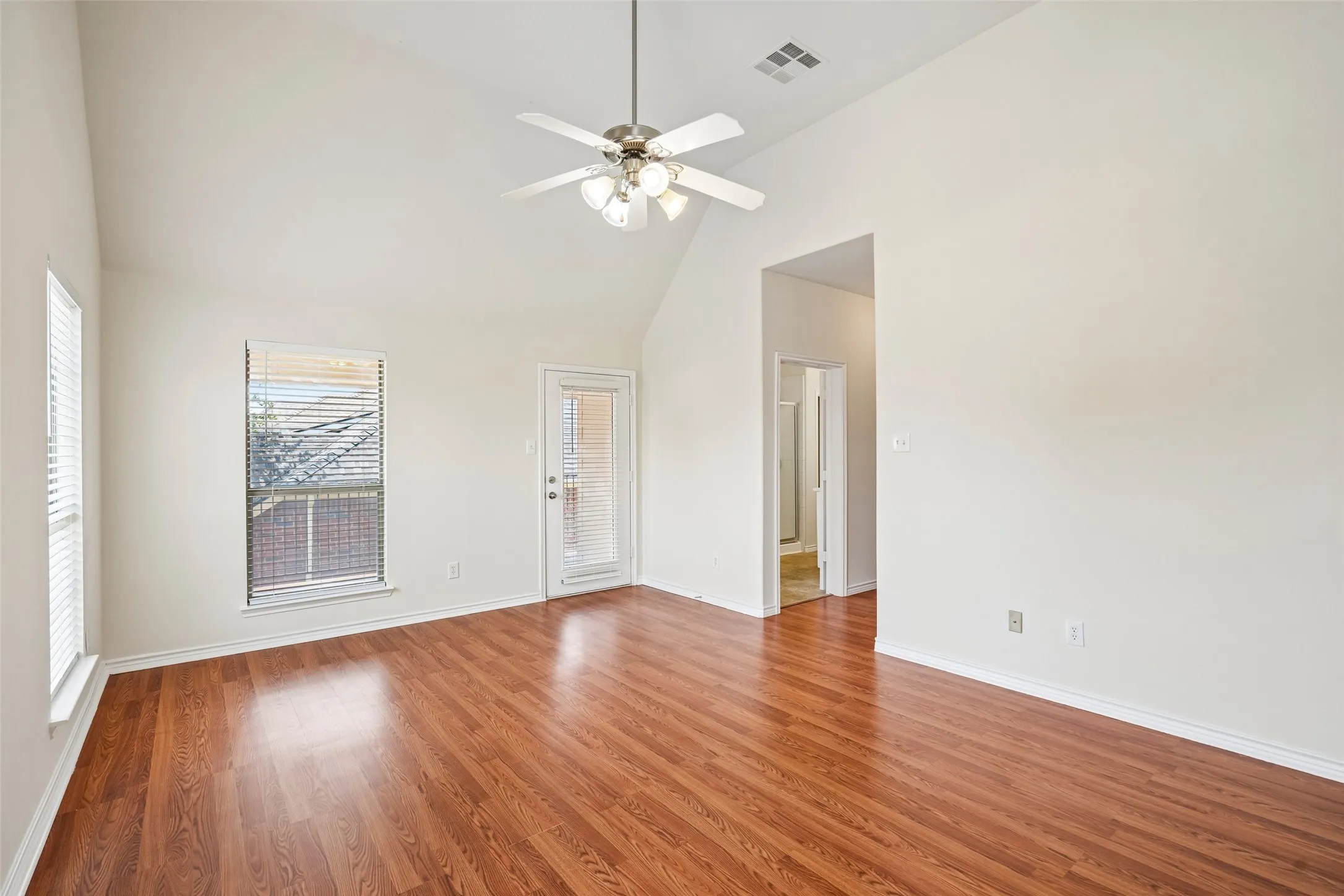 Vaulted ceilings with a multi-blade light fixture, wood-finish flooring, and a glass-paneled exterior door