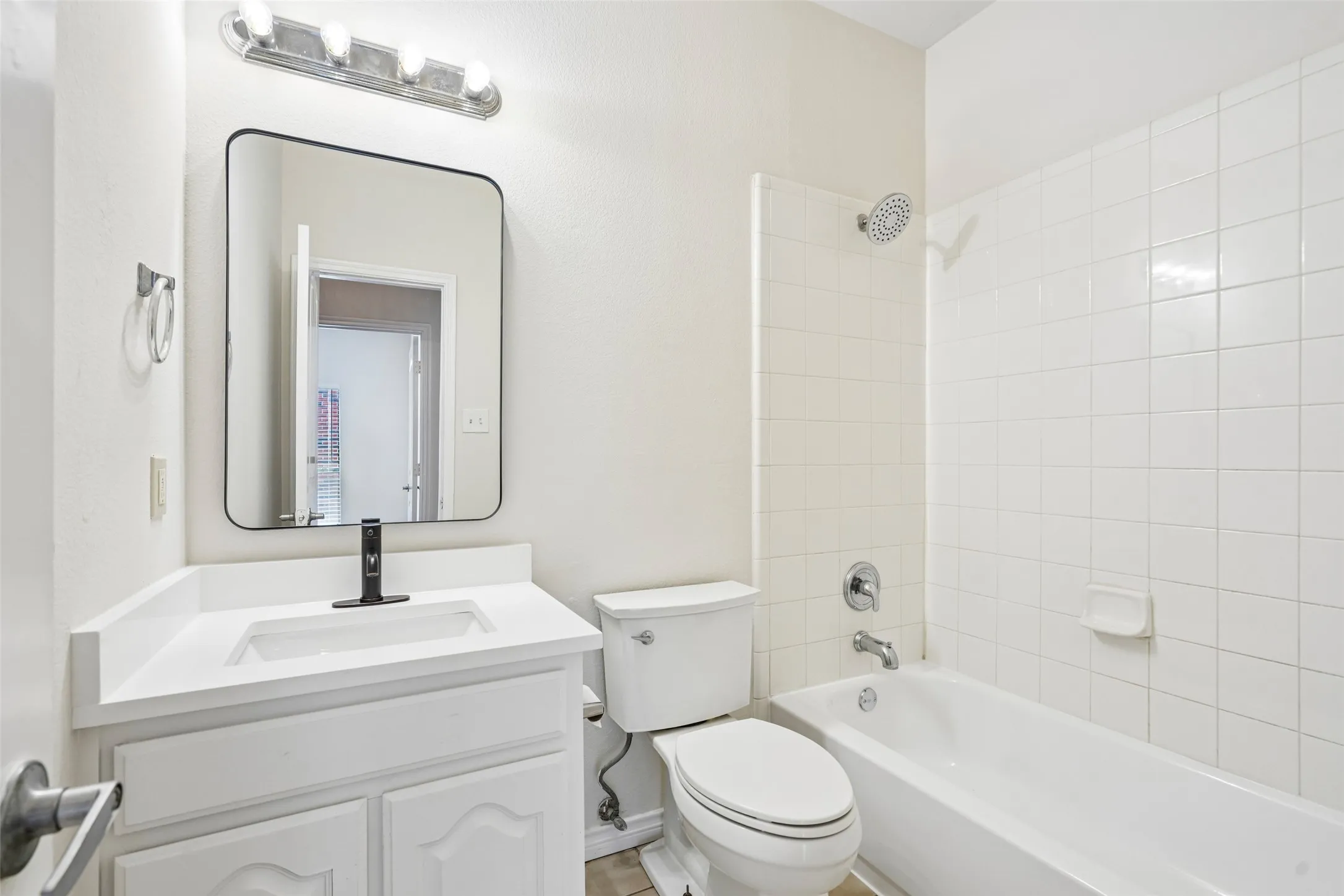 Bathroom featuring a vanity with a white countertop and rectangular sink, a black high-arc faucet, a rectangular mirror with rounded corners, and a tiled shower-tub combination