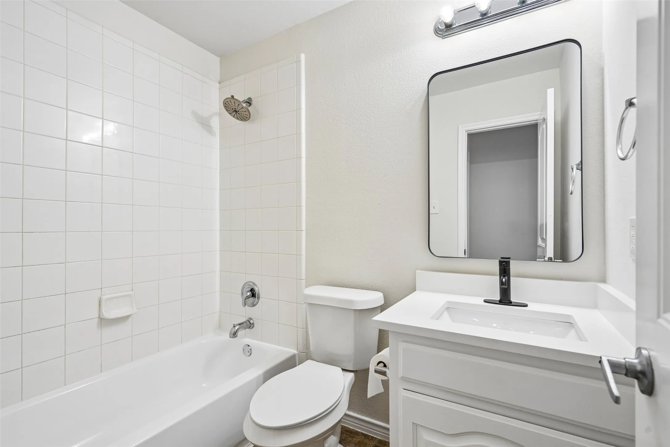 Bathroom featuring a white vanity with an integrated basin, a matte black single-handle faucet, a rectangular wall-mounted mirror, and a tub-shower combination with white tile surround
