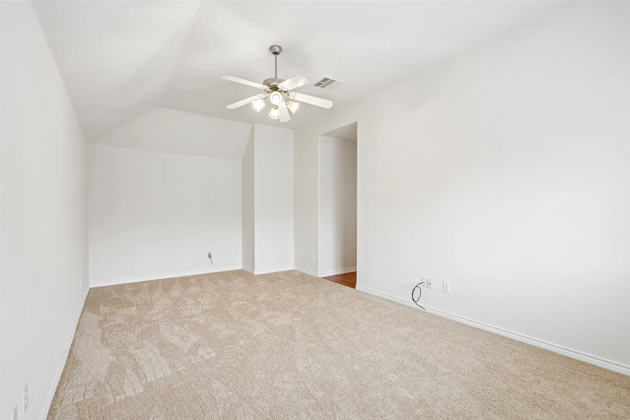 Vaulted ceiling featuring a central brushed-nickel ceiling fan with integrated light kit and neutral wall-to-wall carpeting