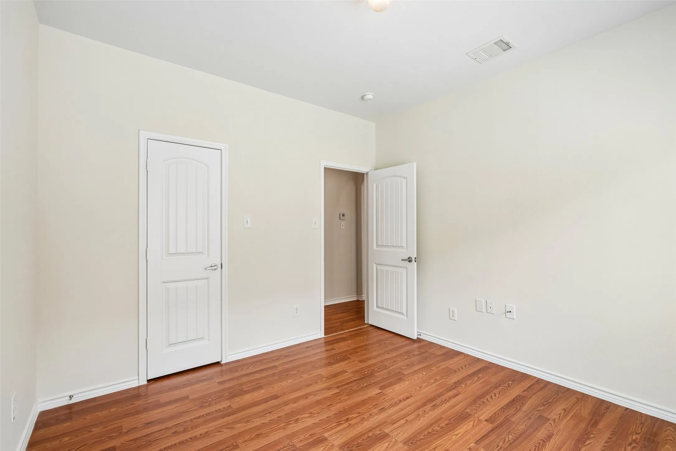 Interior room featuring wood-finish flooring, neutral wall tones, and two-panel interior doors with satin nickel hardware