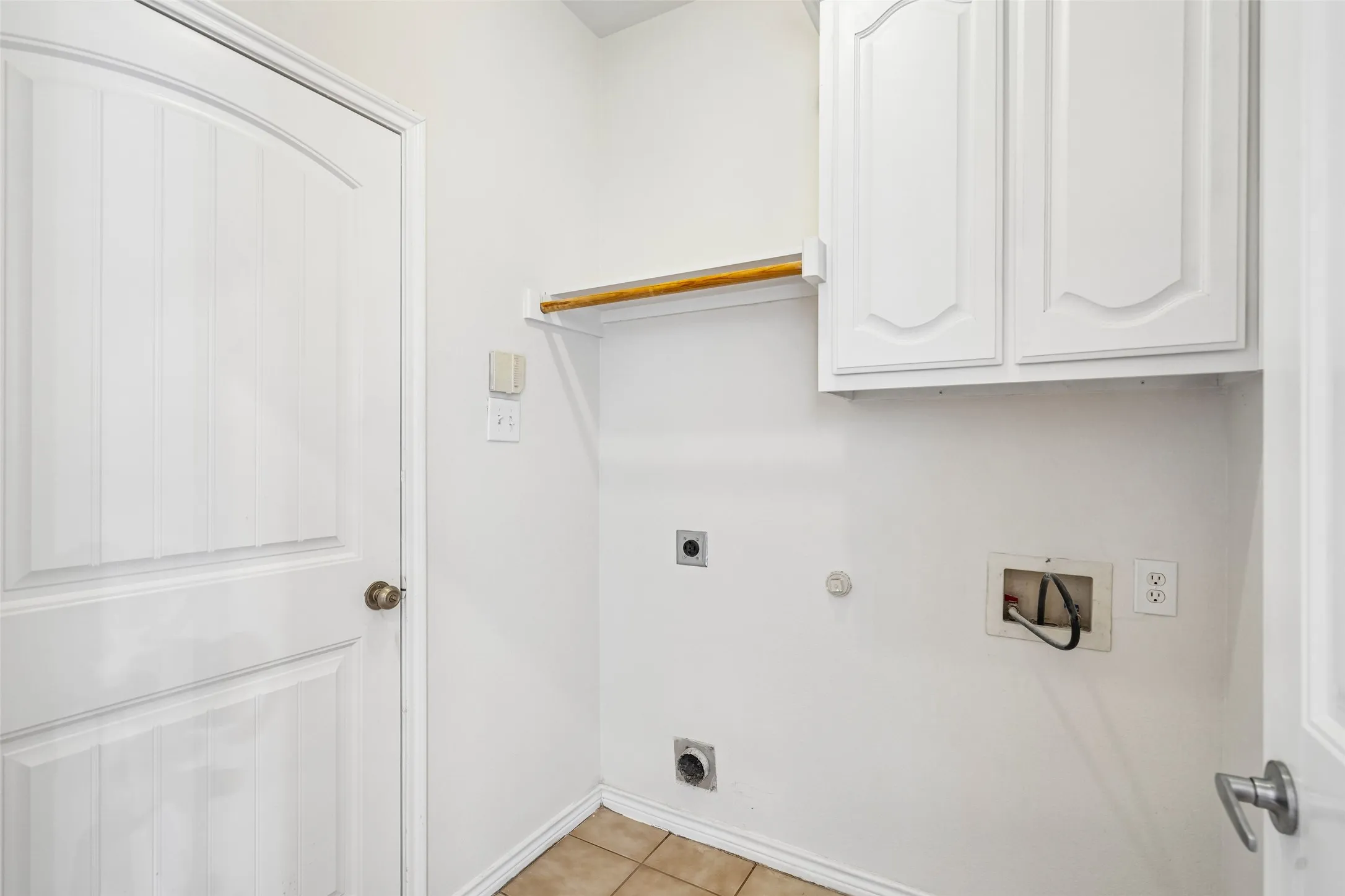 Utility area featuring white raised-panel cabinetry, a wood-finish hanging rod, neutral tile flooring, and standard utility connections