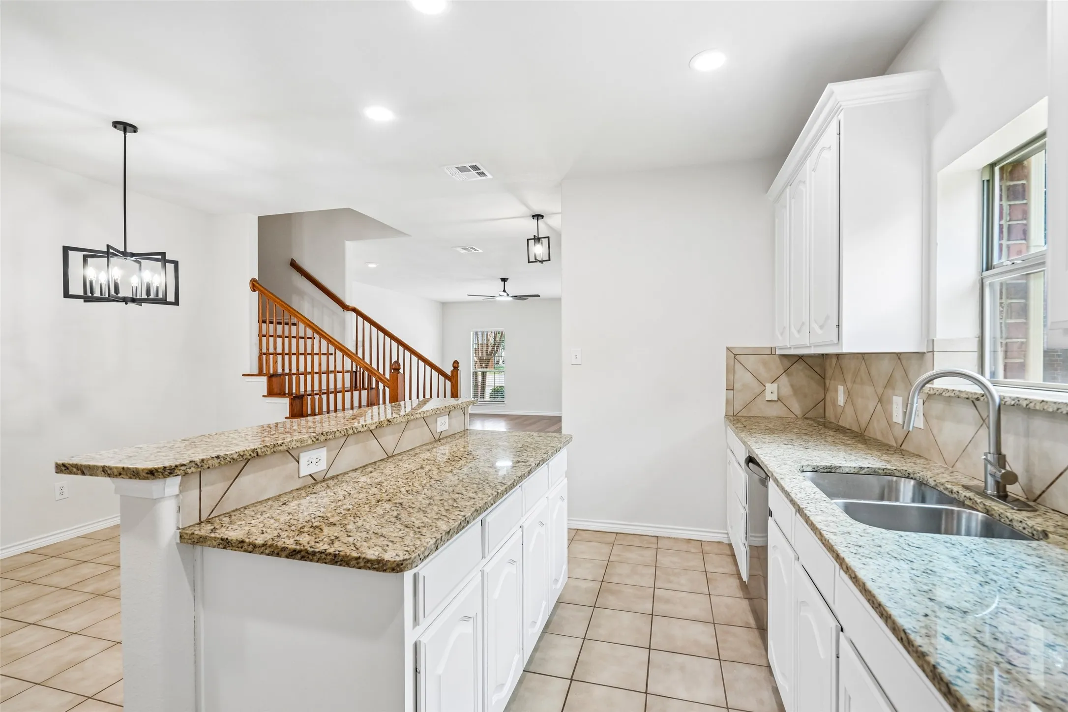 Kitchen featuring stone-finish countertops, white cabinetry, tile backsplash, dual-basin stainless steel sink, and decorative pendant lighting