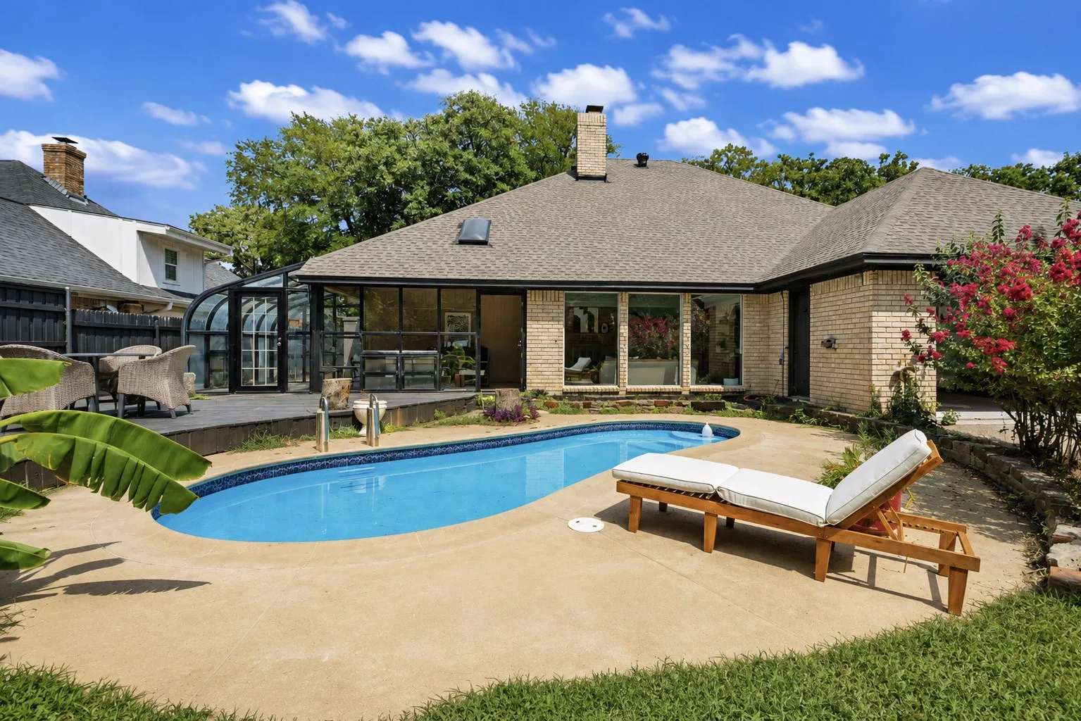 Brick exterior residence featuring an in-ground pool with concrete decking, an attached solarium, and a rear covered patio