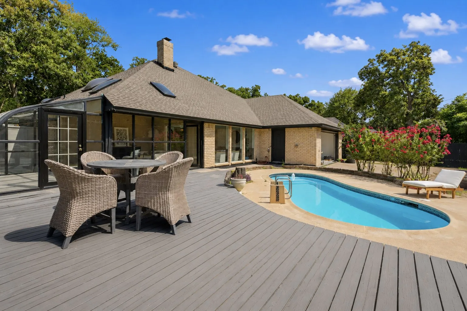 Exterior featuring a multi-level deck, an oval in-ground swimming pool, masonry chimney, roof-integrated skylights, and a glass-enclosed solarium
