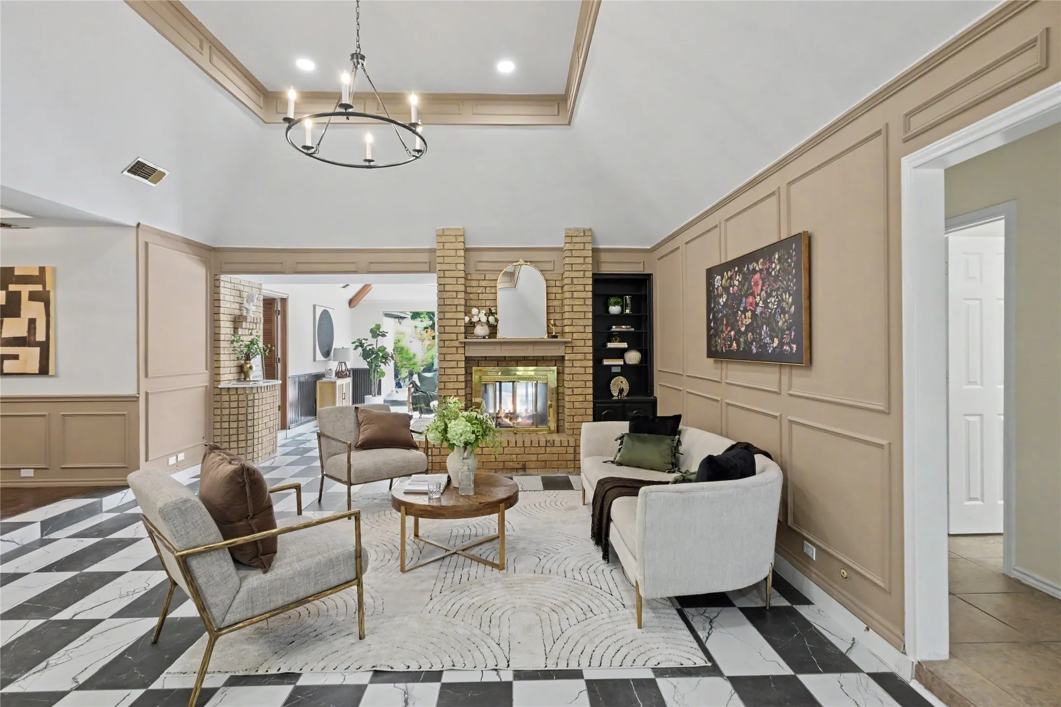 Vaulted ceiling with tray detailing, floor-to-ceiling brick fireplace with integrated shelving, geometric checkered tile flooring, and extensive wall wainscoting