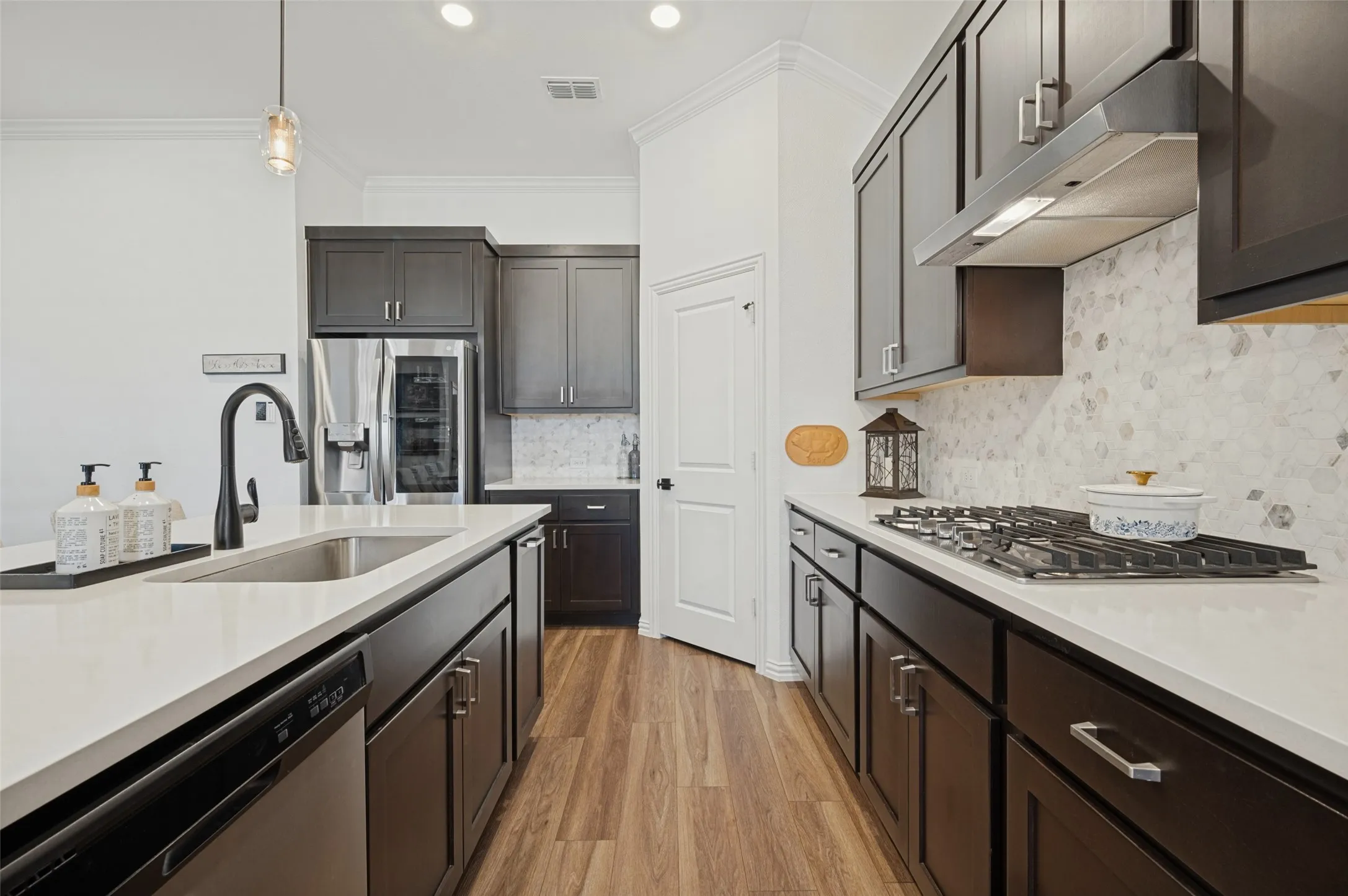Kitchen featuring dark cabinetry, solid-surface countertops, a geometric-pattern backsplash, gas cooktop, and wood-finish flooring
