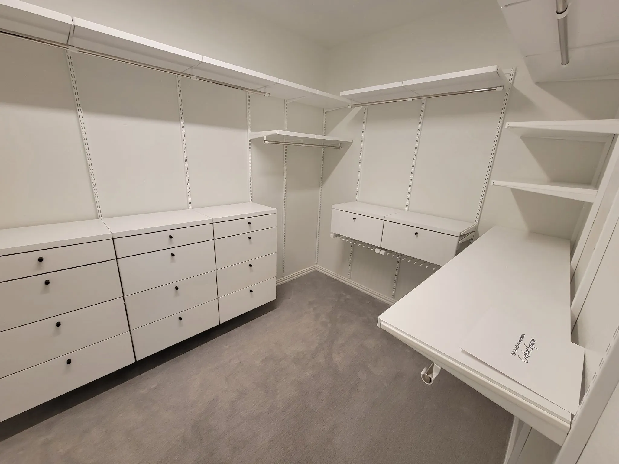 Walk-in closet featuring white built-in cabinetry, integrated drawers, multi-level shelving, metal hanging rods, and carpeting