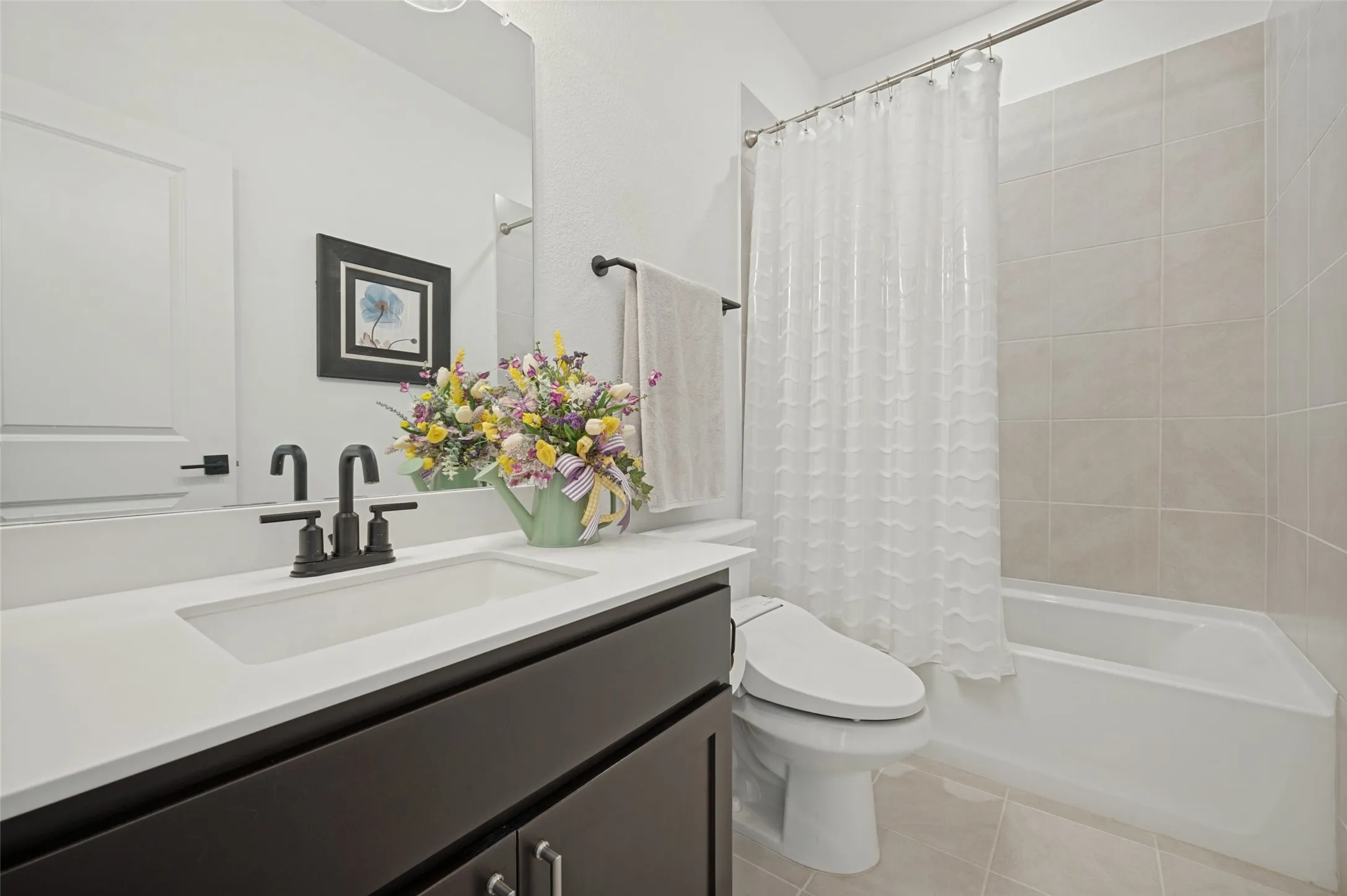 Dark-toned vanity with a rectangular sink, crisp white countertop, matte black faucet, and a tub-shower combination featuring neutral wall tiling