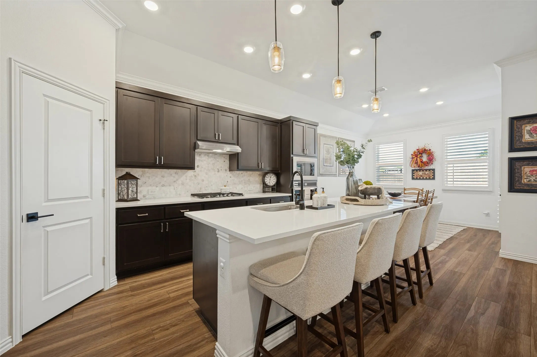 Kitchen featuring dark wood cabinetry, quartz countertops, a stone-patterned backsplash, wood-finish flooring, and pendant lighting