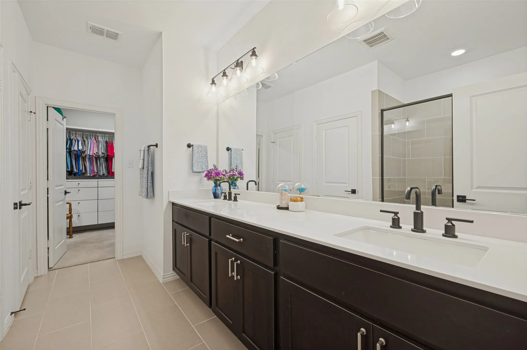 Double vanity featuring dark cabinetry, solid-surface white countertops, rectangular undermount sinks, matte black widespread faucets, and a full-width mirror