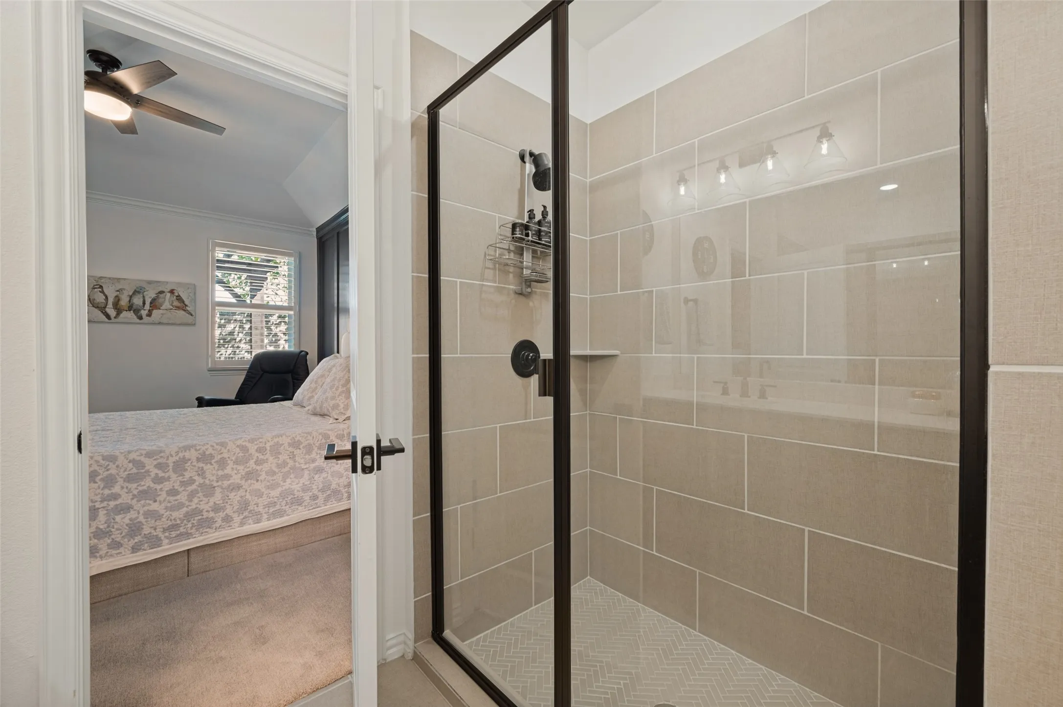Walk-in shower featuring large-format beige wall tile, herringbone-patterned floor tile, matte black hardware, and a glass enclosure with a black frame