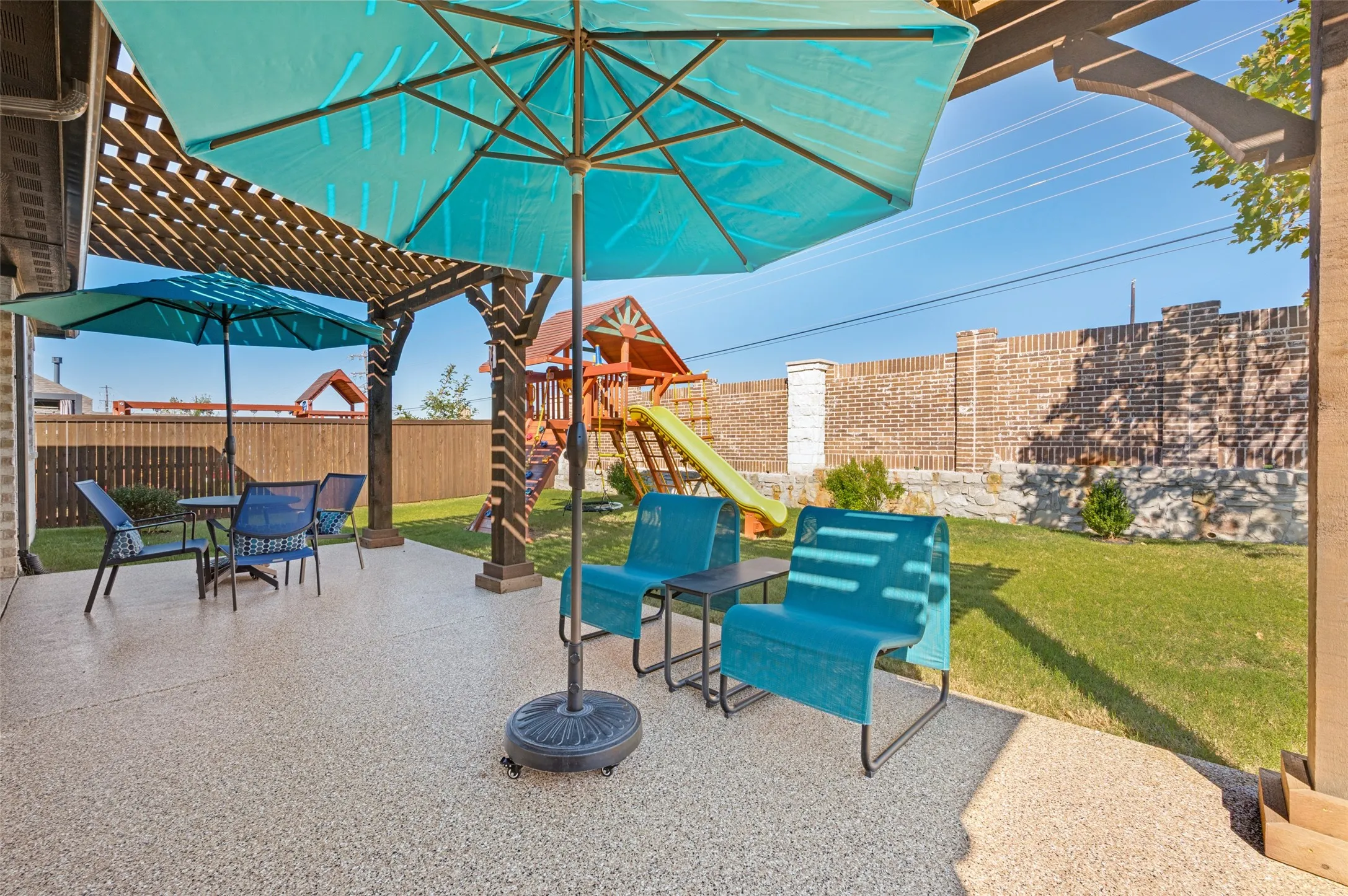 Covered patio featuring a textured concrete finish, overhead timber pergola, brick perimeter wall, and a grass lawn