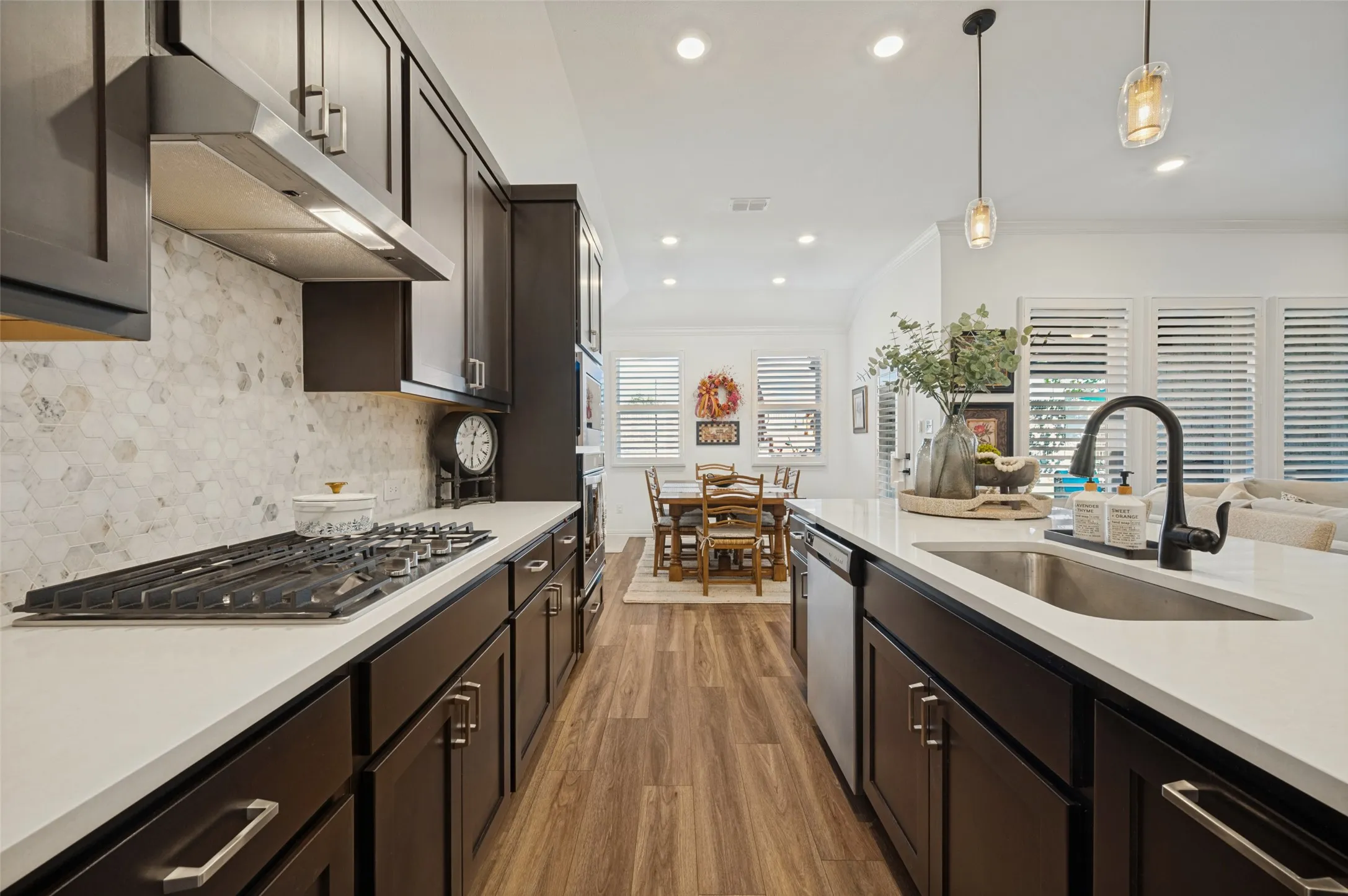 Kitchen featuring dark cabinetry, quartz countertops, a stone-tile backsplash, stainless steel gas cooktop, and wood-finish flooring