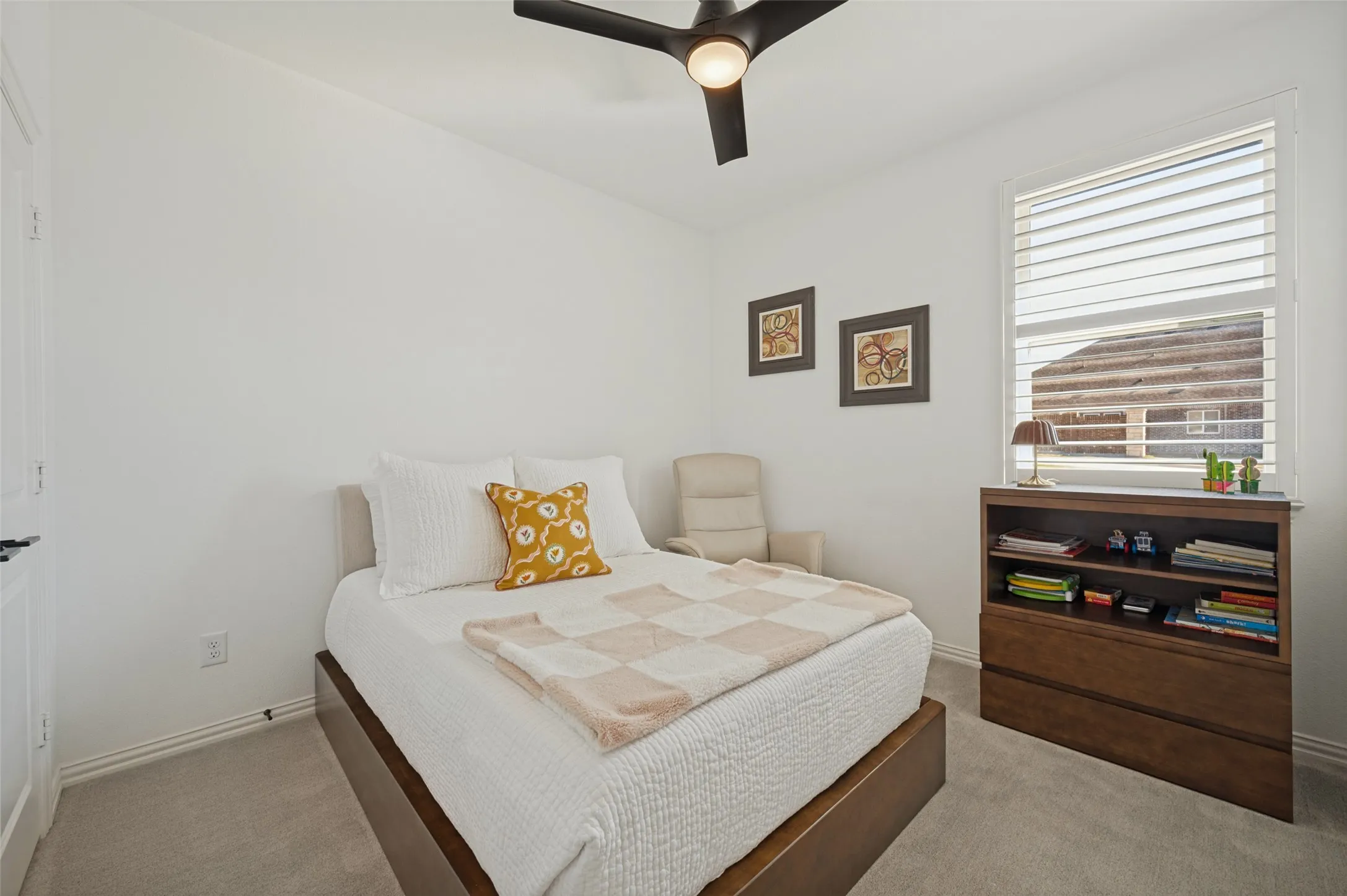 Neutral-toned wall-to-wall carpeting, window fitted with adjustable plantation shutters, and a central ceiling fan with integrated lighting
