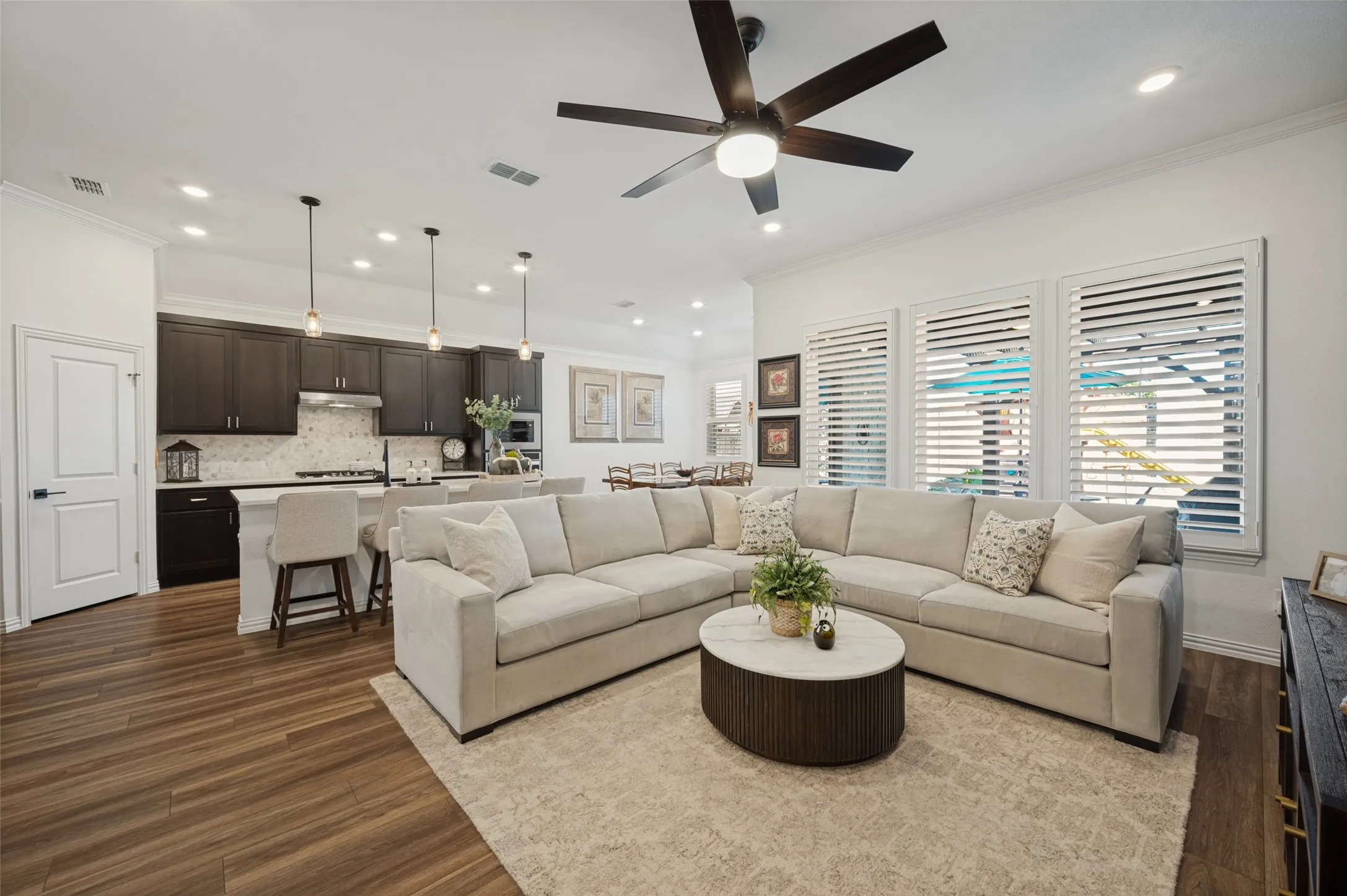 Open-concept living space featuring wood-finish flooring, recessed lighting, and a kitchen equipped with dark cabinetry and a central island