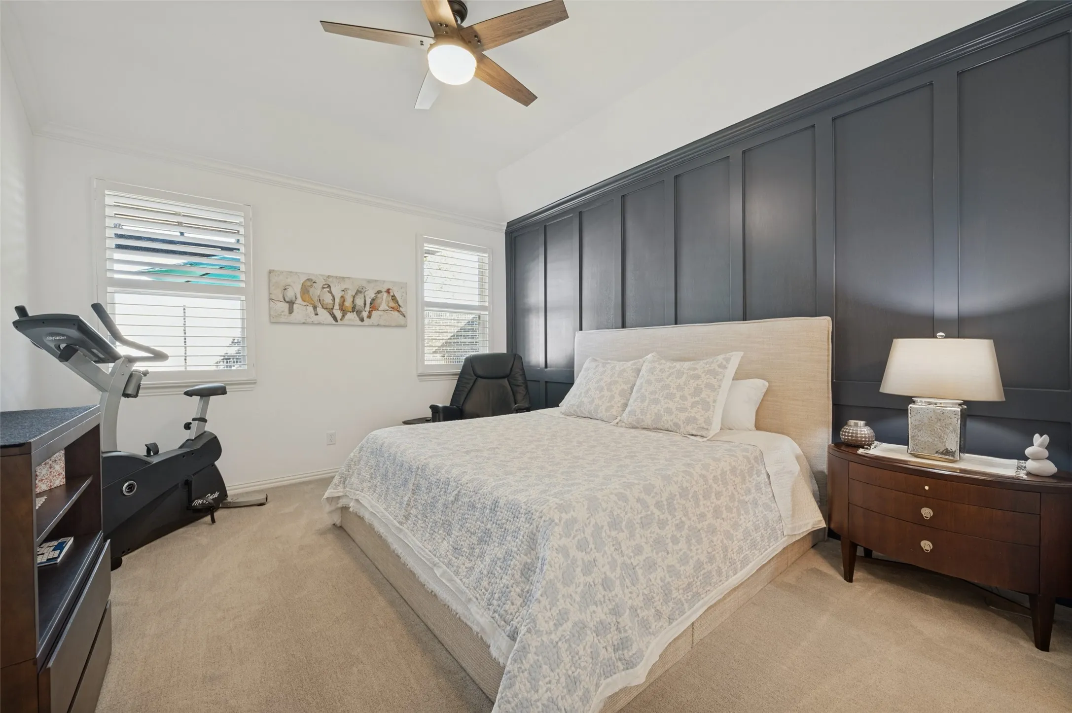 Room featuring floor-to-ceiling dark-toned paneling, wall-to-wall carpeting, dual windows with plantation shutters, and a ceiling fan with integrated lighting
