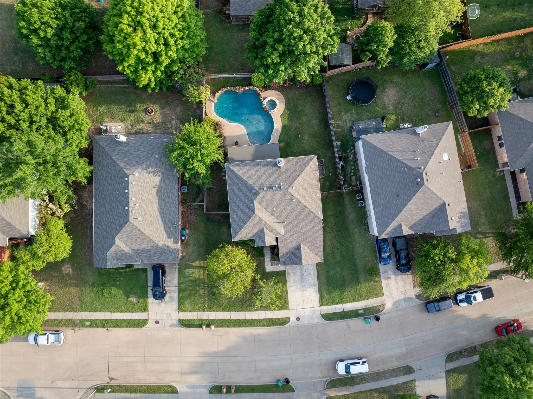 Aerial perspective of property featuring an in-ground swimming pool, attached spa, concrete patio, and established trees within a fenced backyard