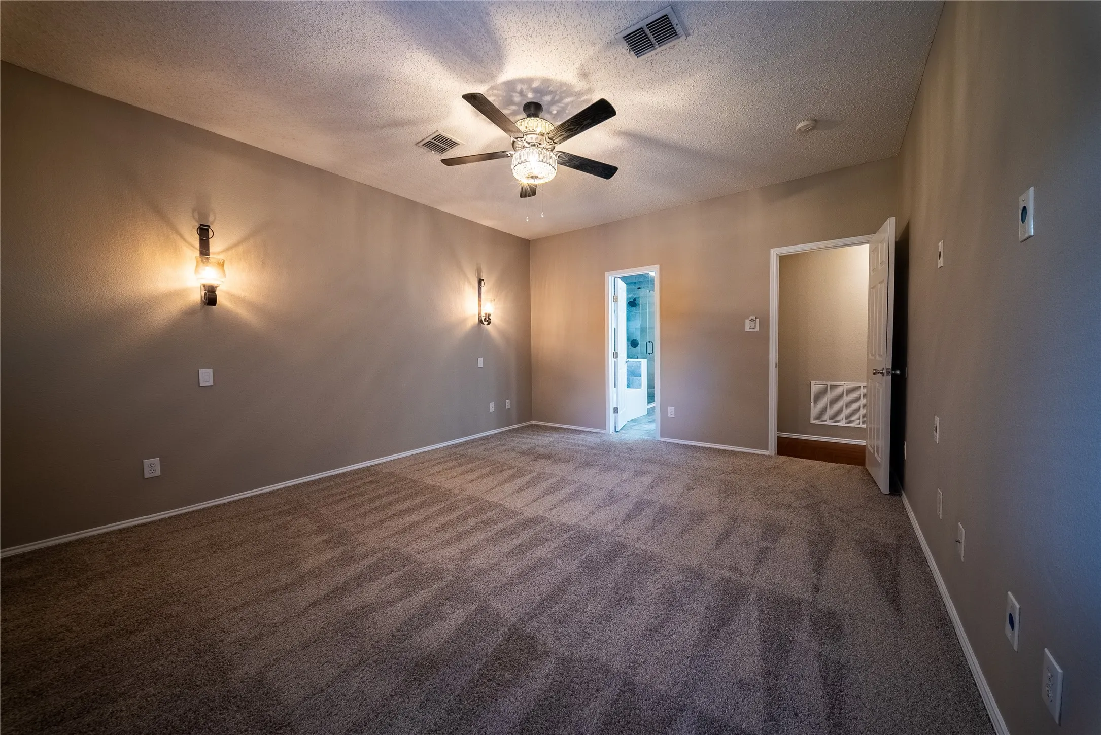 Interior space featuring neutral wall tones, textured carpeting, a multi-blade ceiling fan with integrated lighting, and dual wall-mounted light fixtures