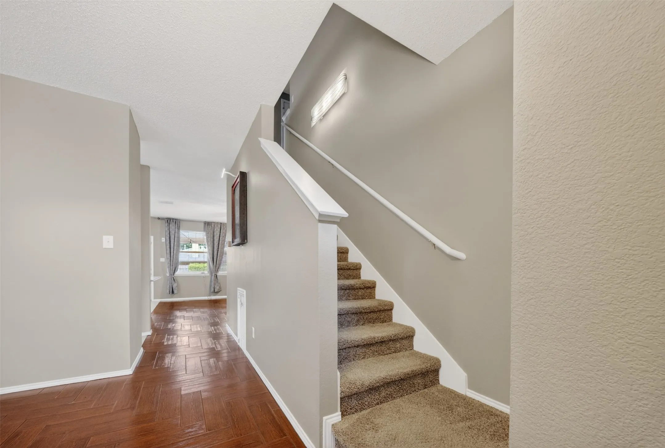 Staircase featuring carpeted treads, a white handrail, and a half-wall partition, complemented by wood-finish flooring in a herringbone pattern