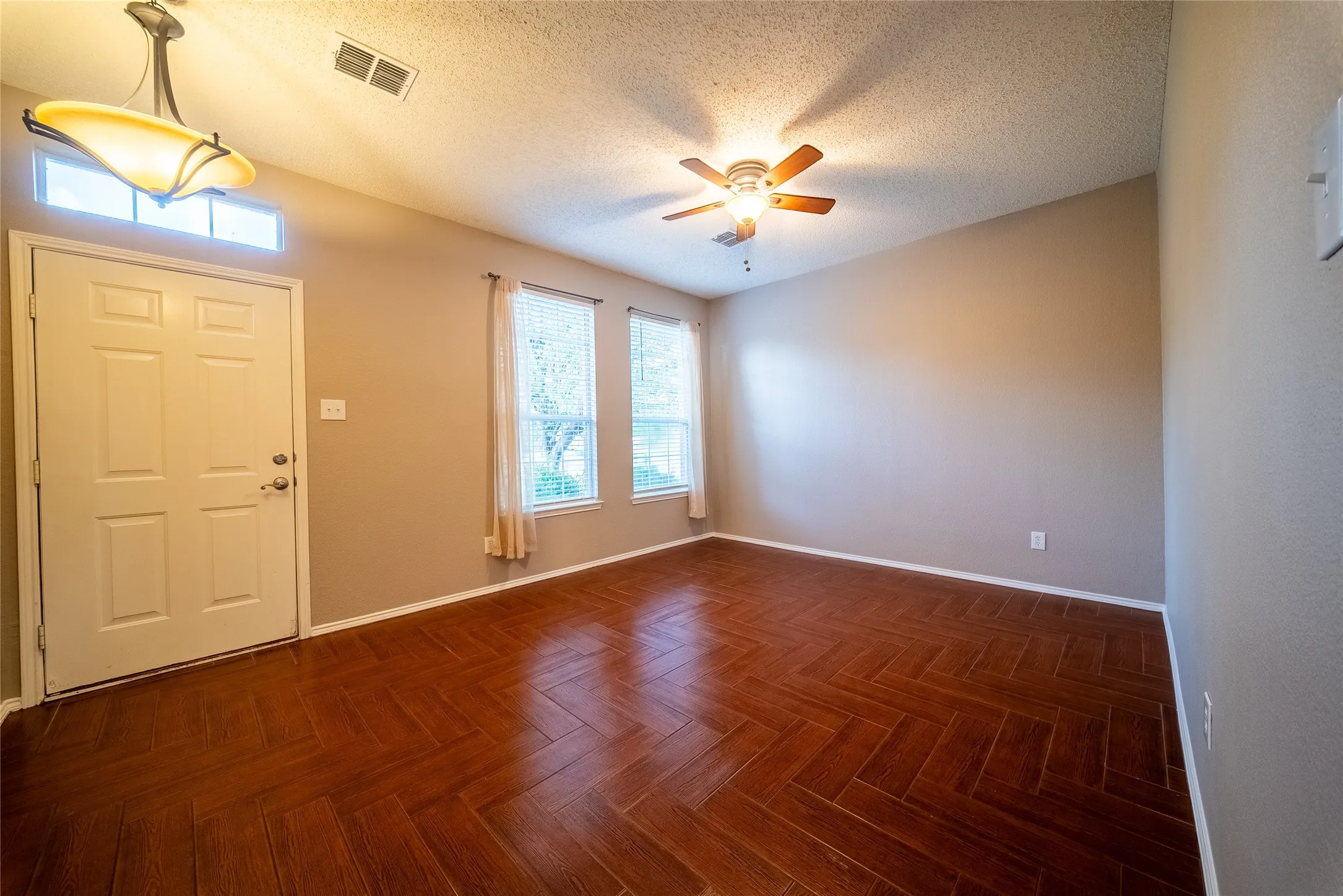 Herringbone-pattern wood-finish flooring, multi-pane entry door with transom window, suspended pendant light fixture, and ceiling fan with integrated lighting