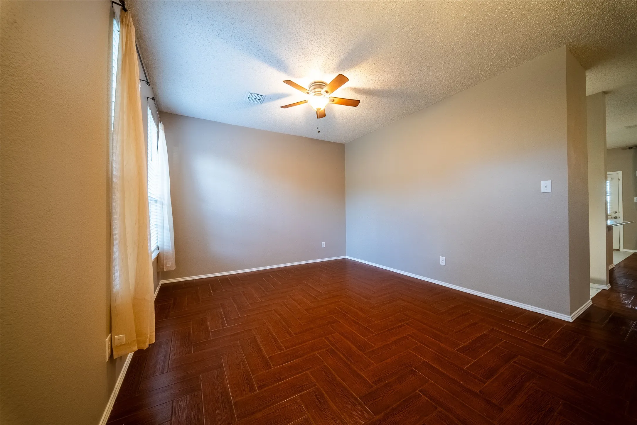 Wood-finish flooring arranged in a herringbone pattern, neutral wall paint, and a ceiling-mounted fan with light fixture