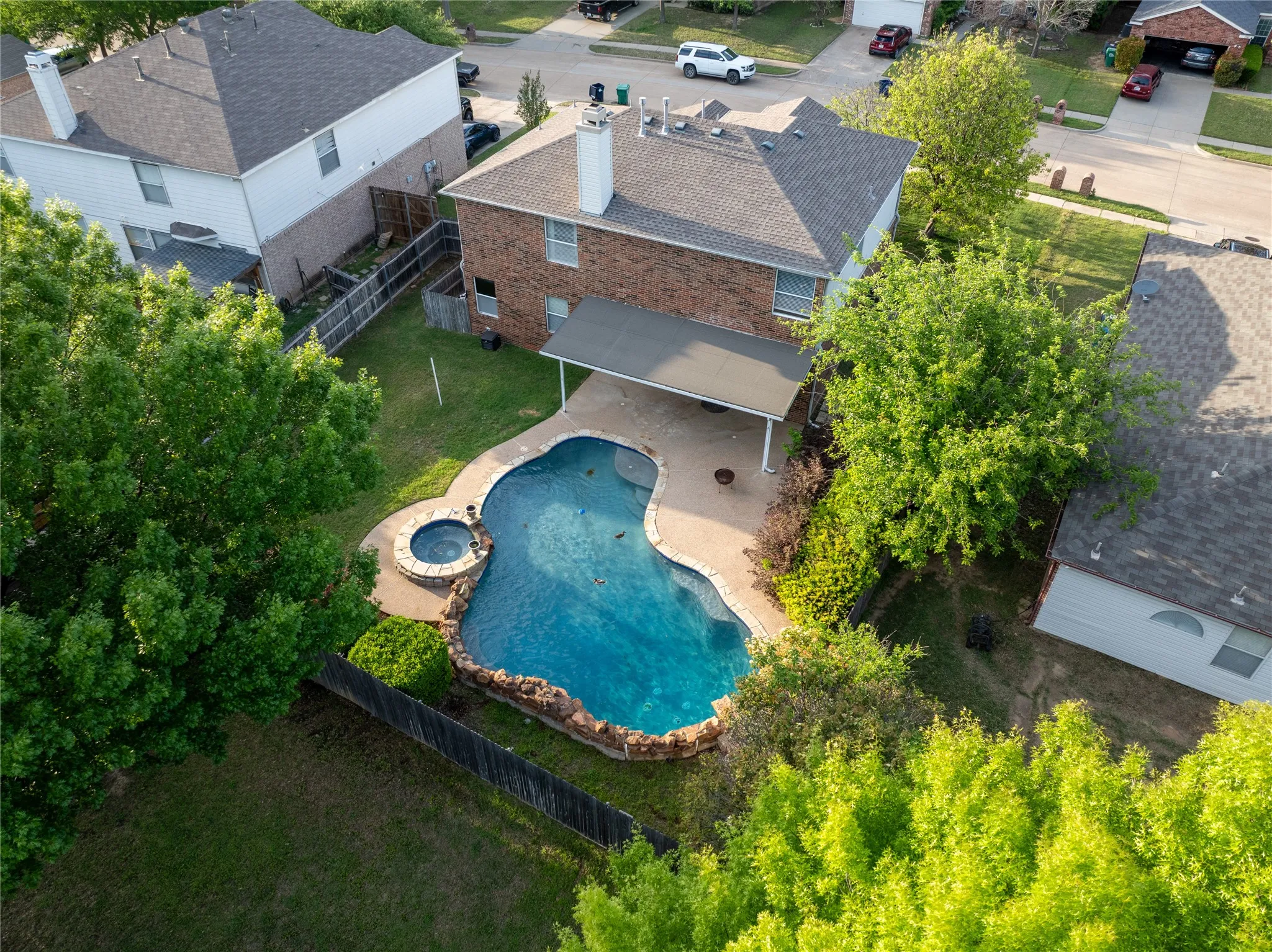 Two-story brick exterior with a covered rear patio, swimming pool with stone-accented perimeter, and integrated spa