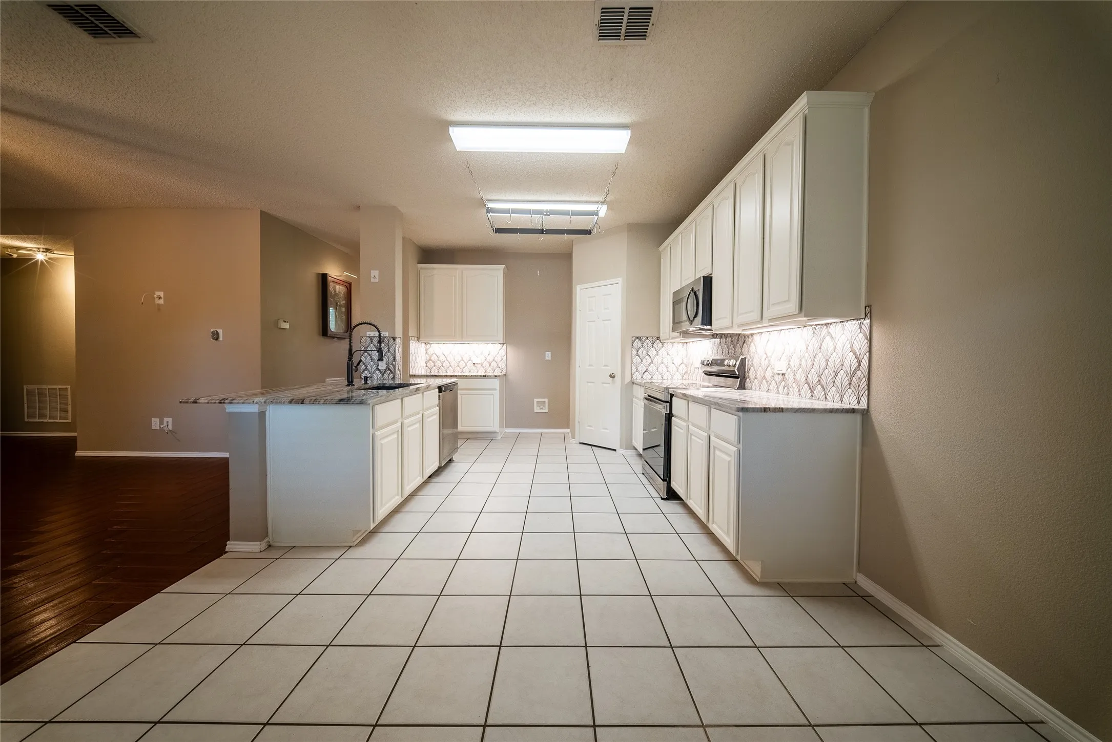 Kitchen featuring white cabinetry, patterned tile backsplash, stone-finish countertops, stainless steel appliances, and large-format tile flooring