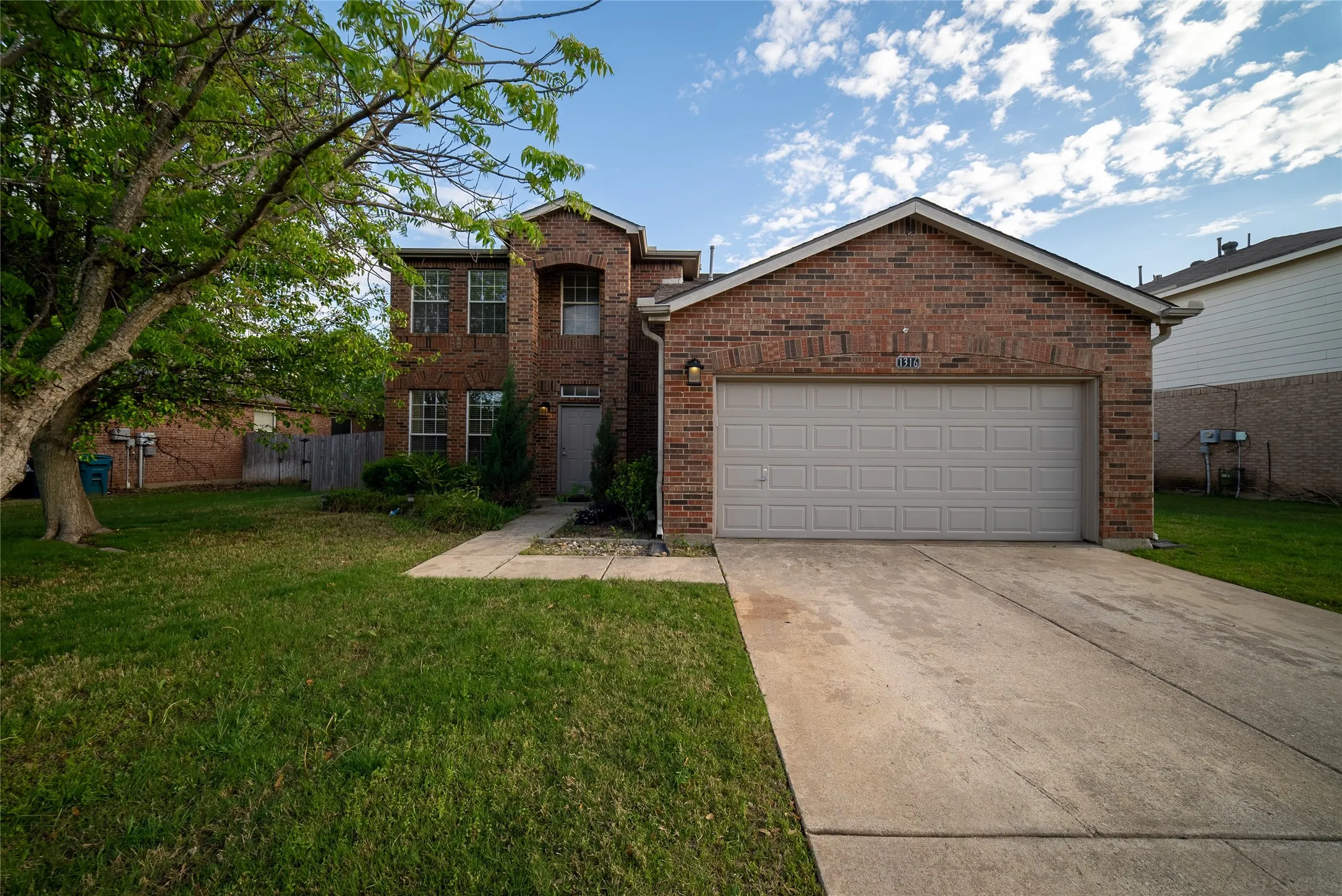 Two-story brick exterior featuring a multi-gabled roofline, concrete driveway, and attached two-car garage