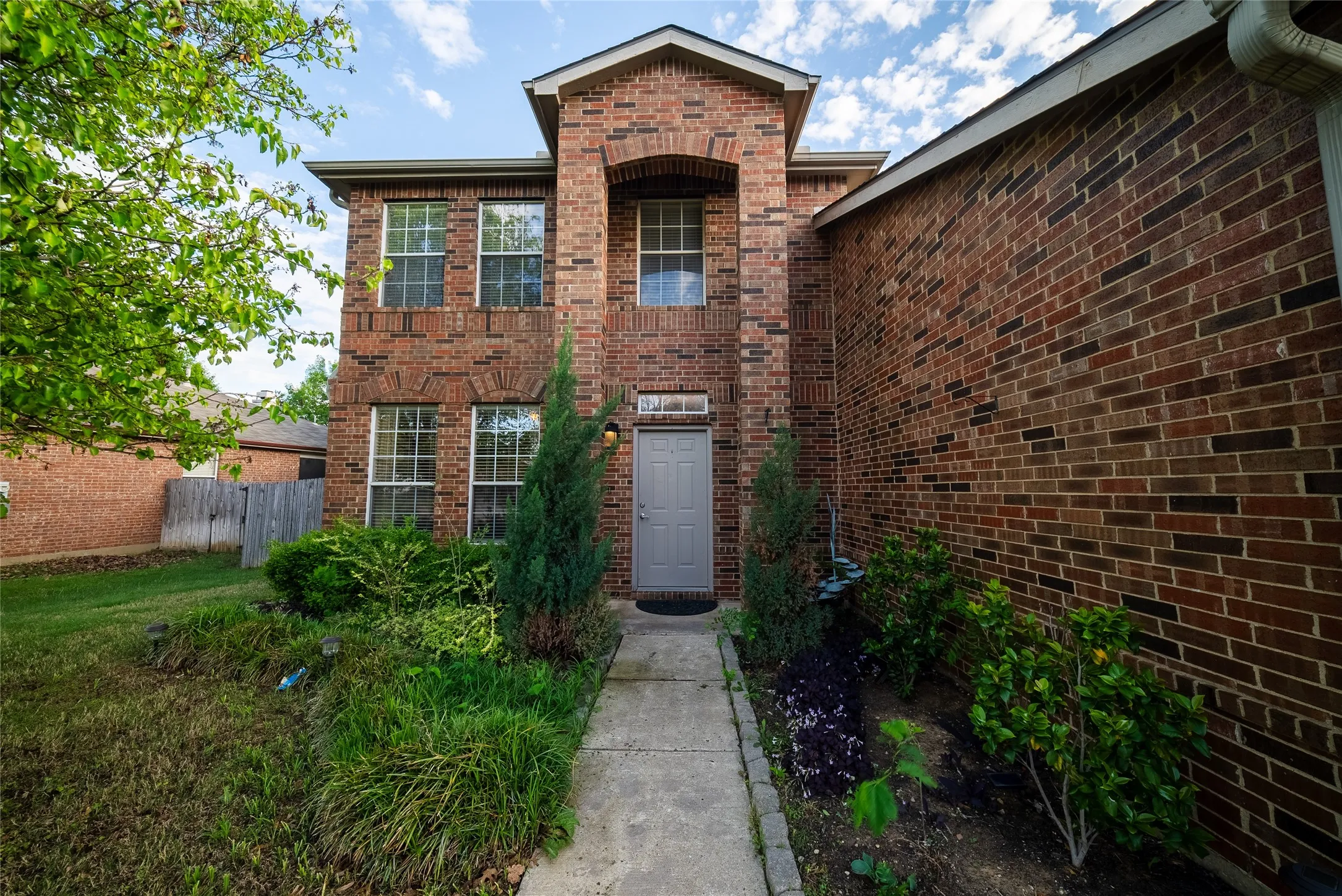 Two-story brick exterior featuring a recessed entryway, an arched portico, multi-pane windows, and a paved walkway