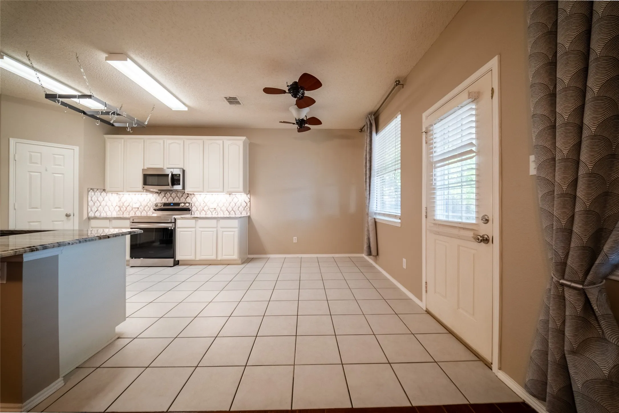 Kitchen featuring white cabinetry, stainless steel appliances, patterned tile backsplash, stone-top breakfast bar, and tile flooring