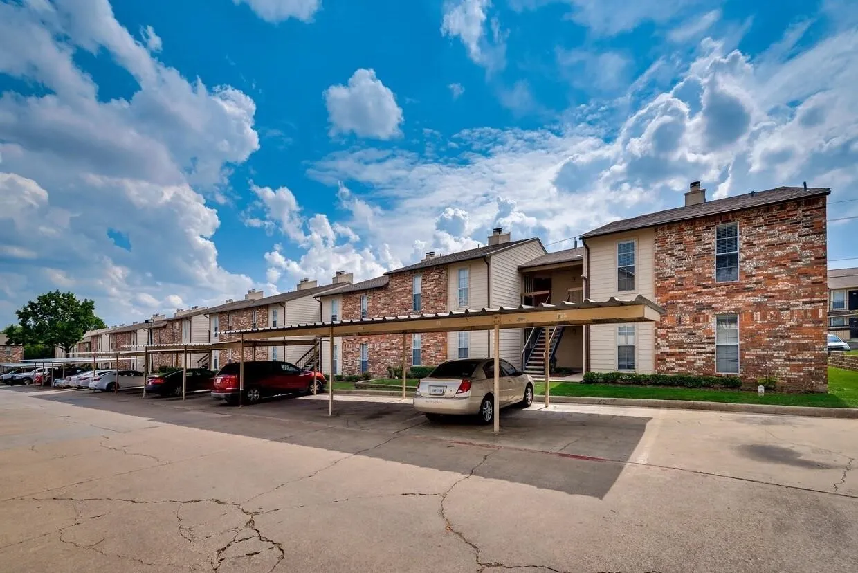 Exterior façade featuring multi-toned masonry and siding, metal-roofed covered parking, and concrete paving