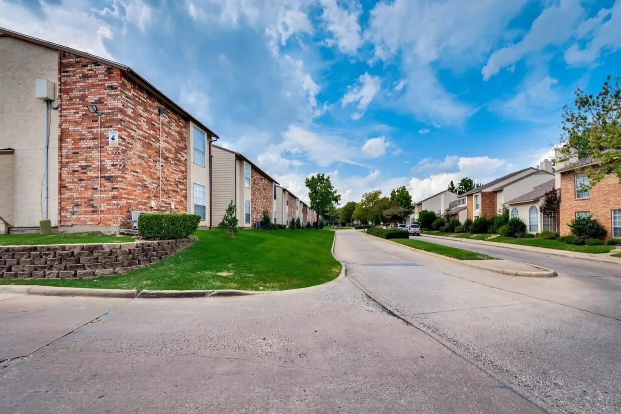 Exterior featuring multi-story brick and siding facades, concrete roadway, retained landscaping, and manicured green space