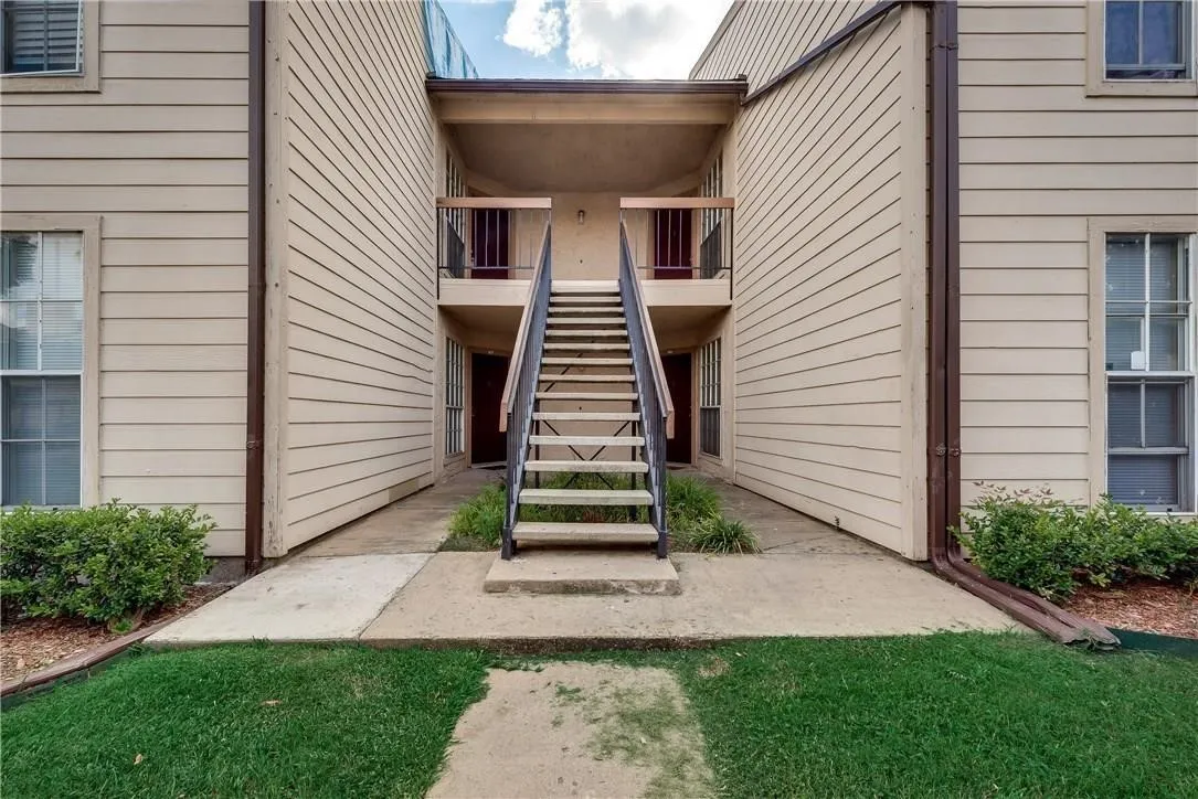 Two-story exterior featuring horizontal lap siding, a central metal staircase with railing, concrete walkway, and multi-pane windows