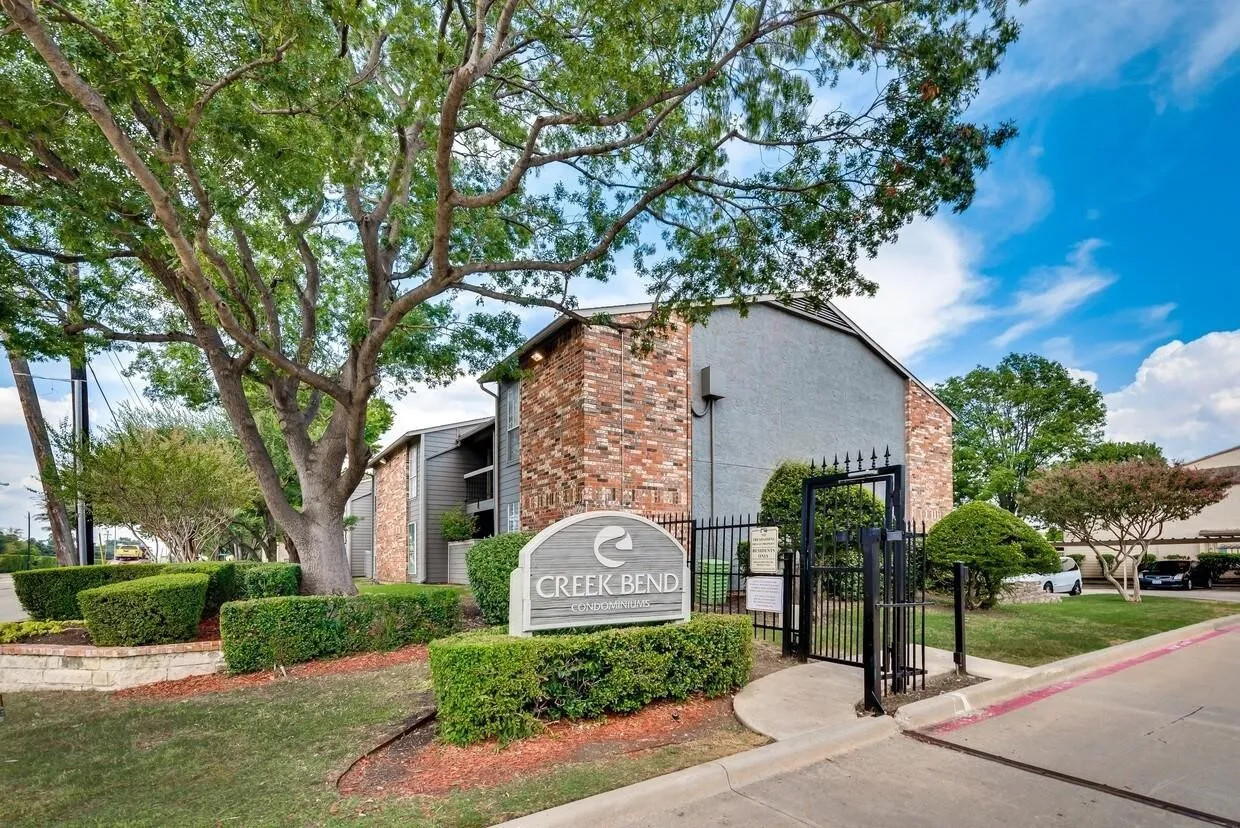 Exterior facade featuring a blend of brick and stucco masonry, mature landscaping, and gated entry