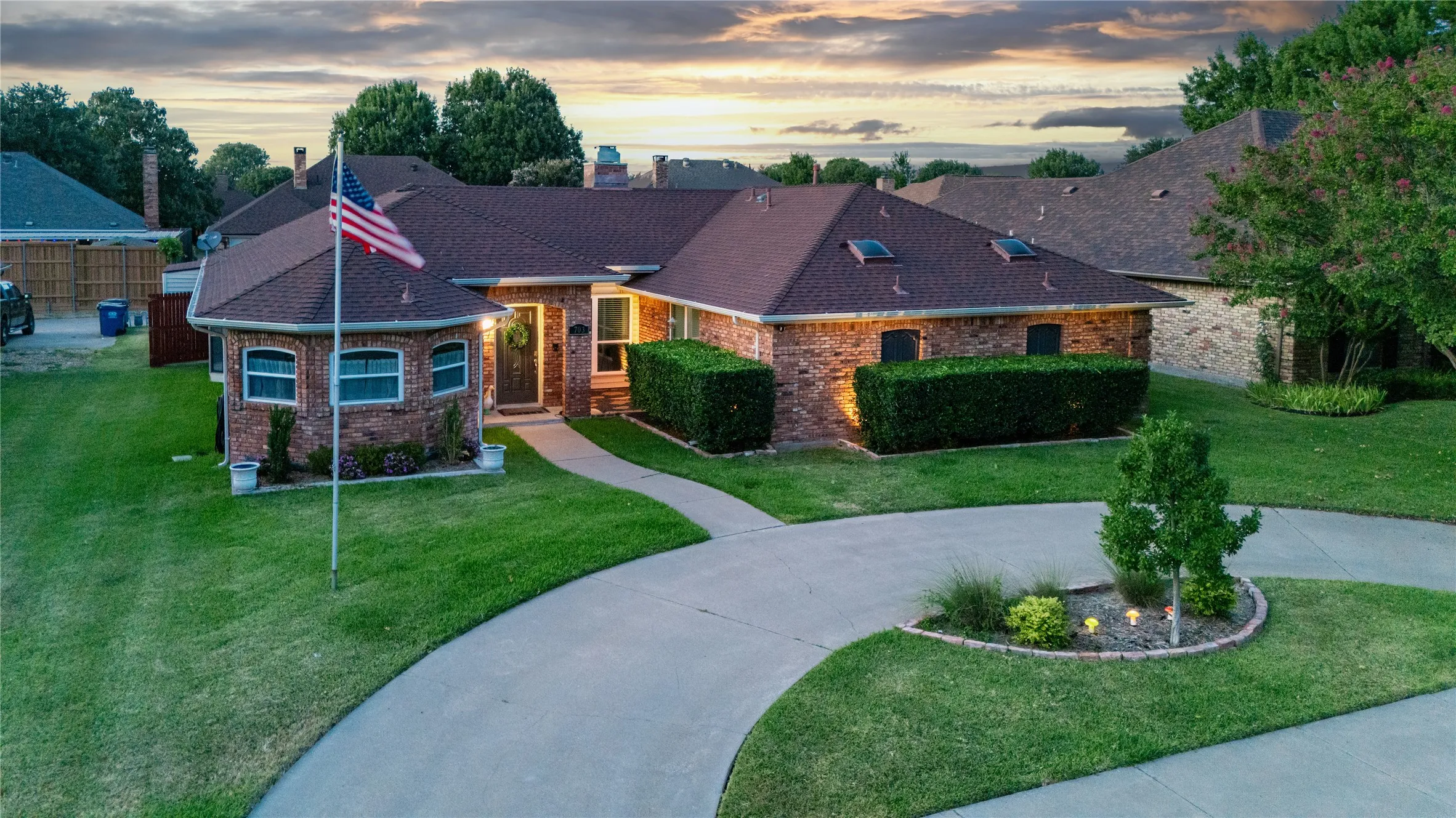 Brick exterior with a brown shingle roof, well-maintained lawn, skylights, and a curved driveway