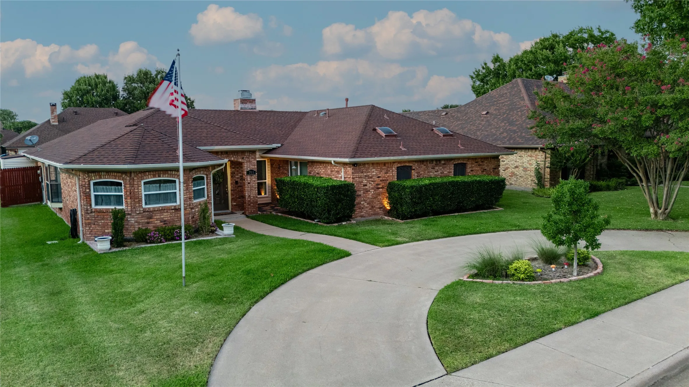 Brick exterior with a brown shingle roof, concrete driveway, and a flag pole