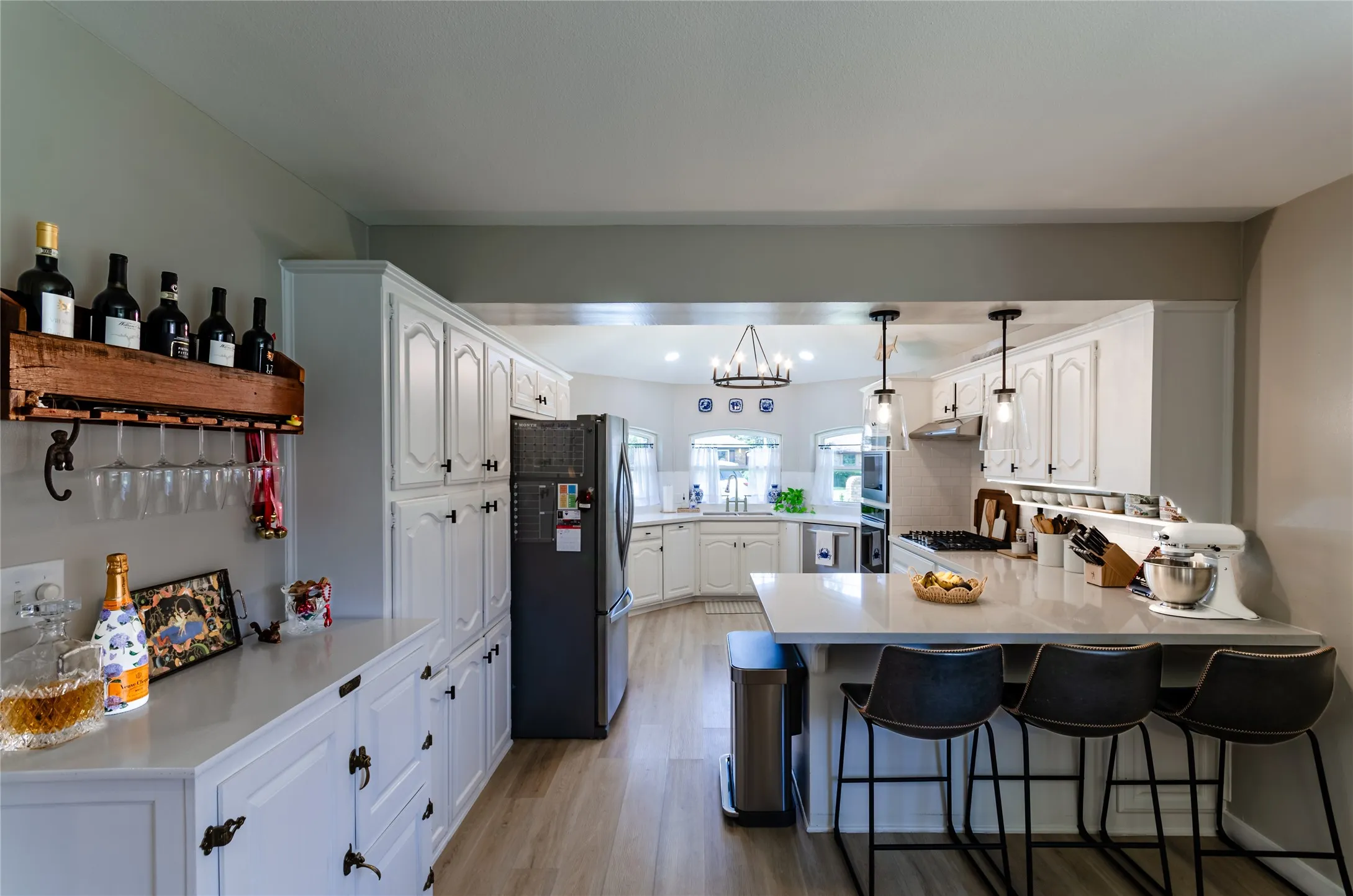 Wood-finish flooring, white cabinetry, integrated refrigerator, pendant lighting, and a kitchen island with seating