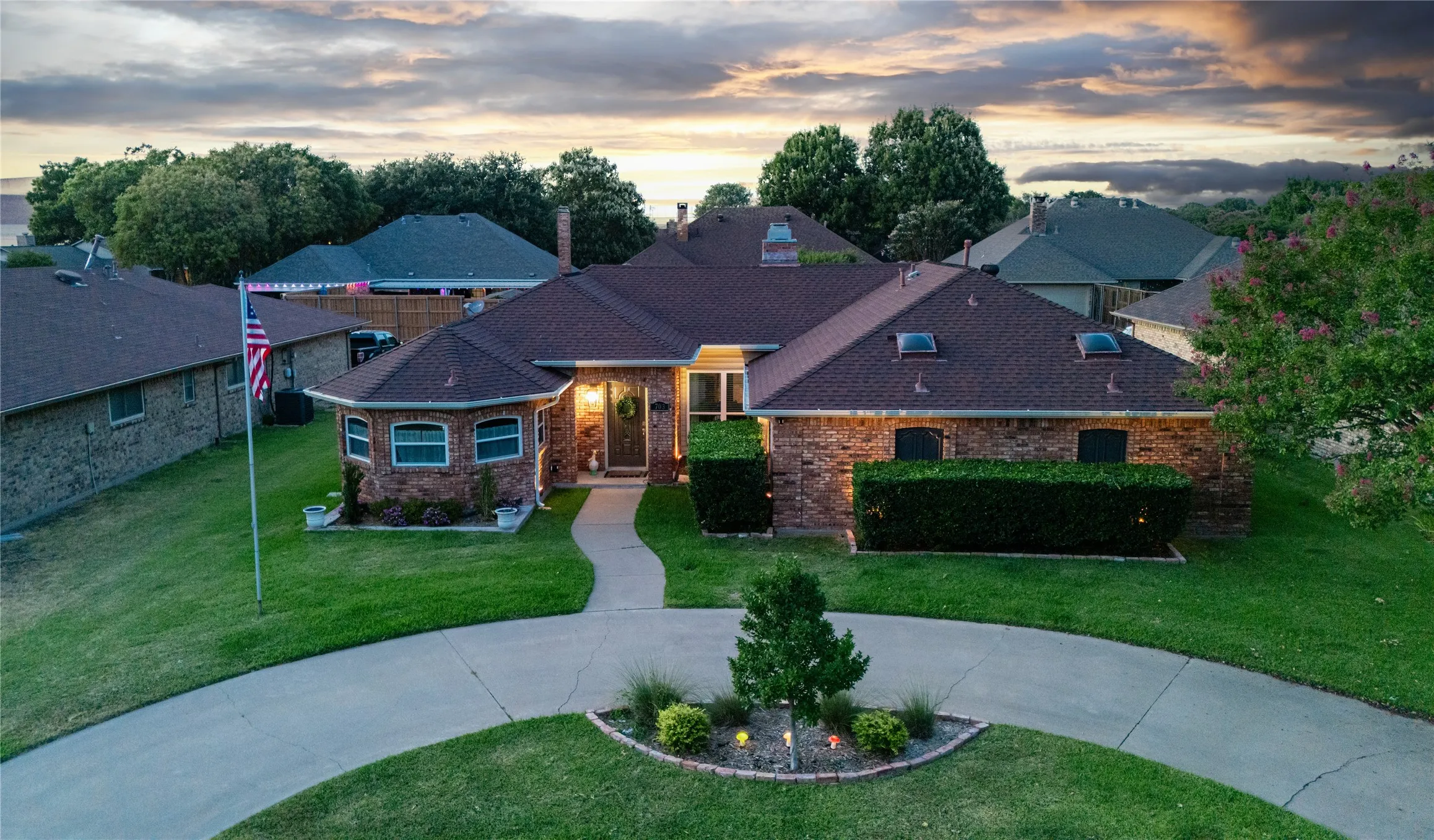 Brick exterior with a brown shingle roof, a circular driveway, a curved walkway, and landscaping