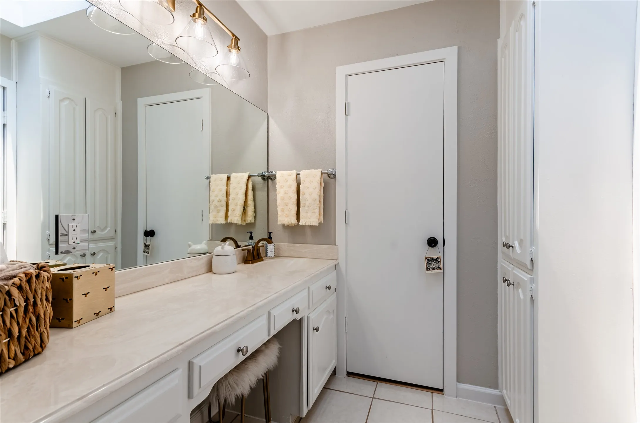 White vanity with integrated countertop, vanity seating area, built-in storage cabinetry, and wall-mounted light fixture