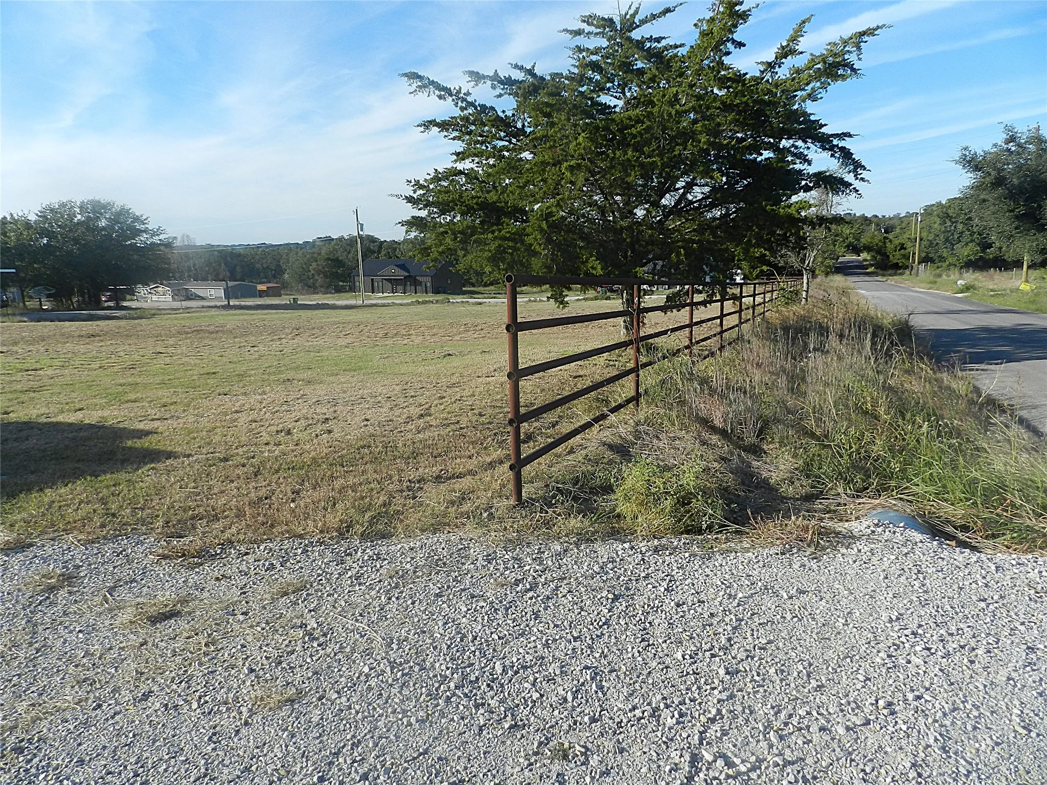 Open acreage featuring a cleared grass lot, mature trees, and a five-rail pipe fence