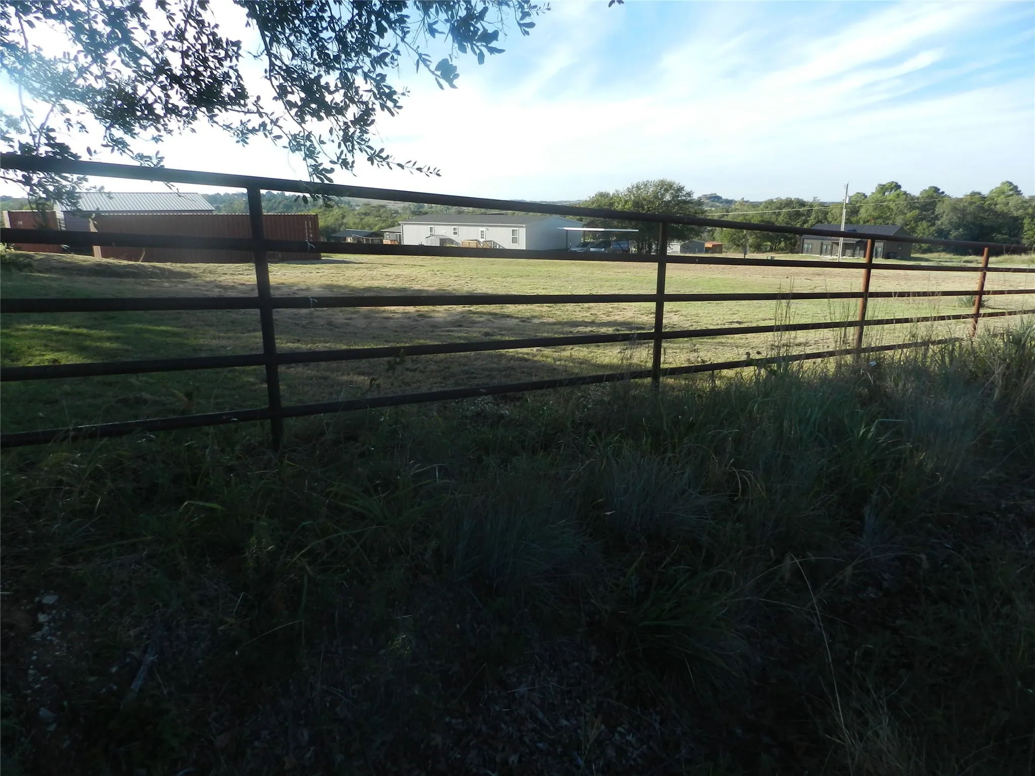 Expansive cleared acreage featuring metal pipe perimeter fencing and multiple auxiliary structures