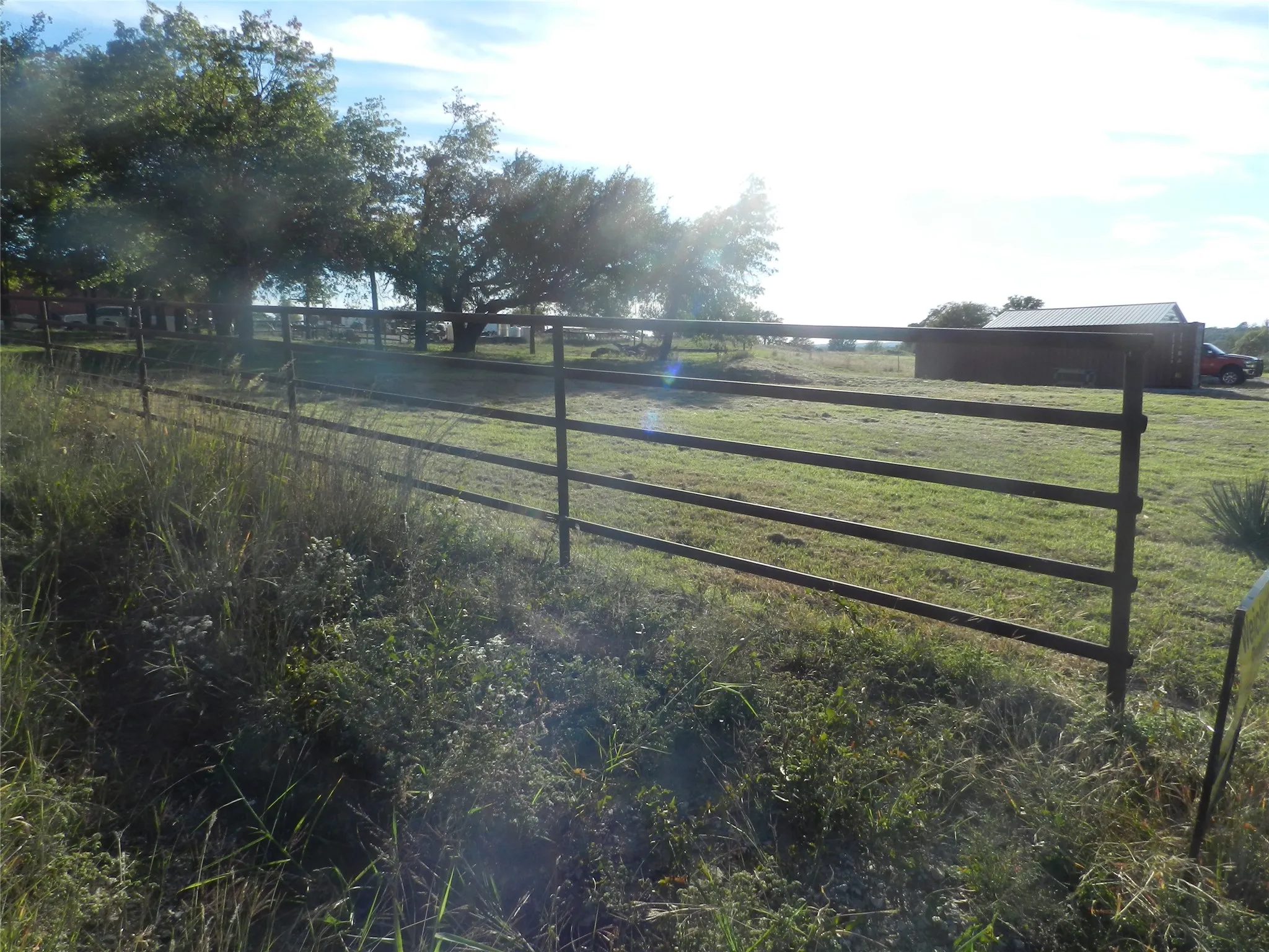 Expansive acreage featuring a multi-rail metal fence, mature trees, and an outbuilding