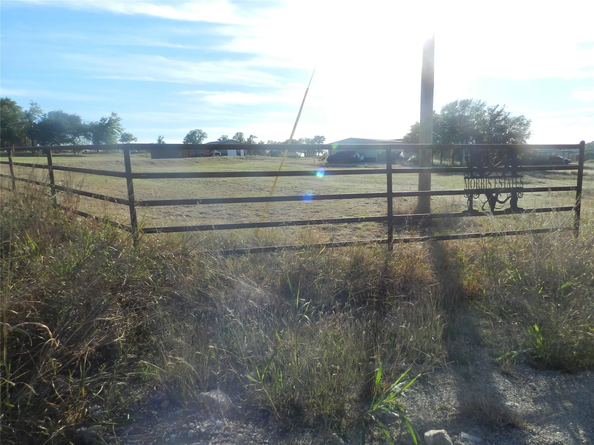 Open acreage lot featuring perimeter metal pipe fencing and custom decorative metal gate signage