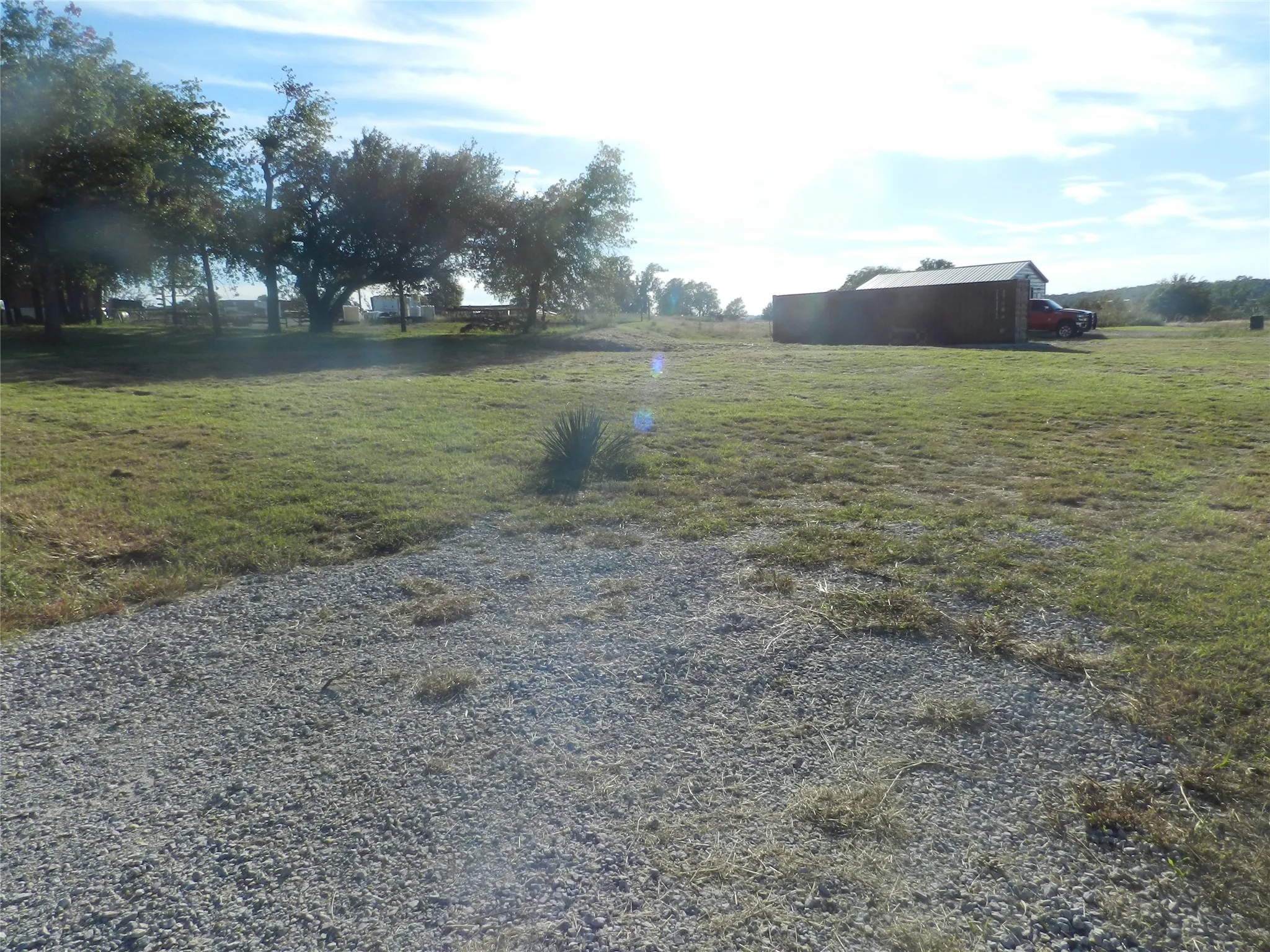 Expansive lot featuring a gravel surface, established mature trees, and a detached metal-sided storage structure
