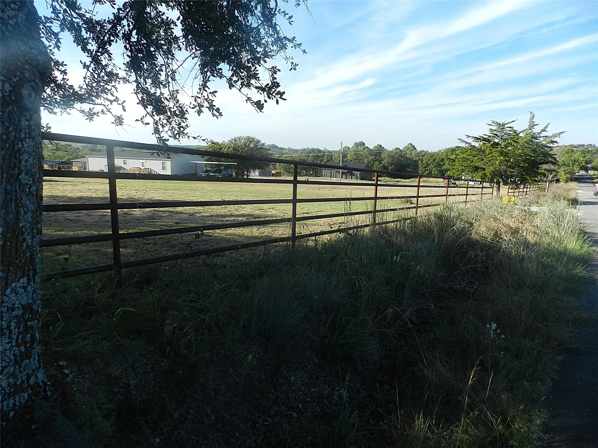 Expansive open acreage featuring multi-rail metal perimeter fencing and mature trees